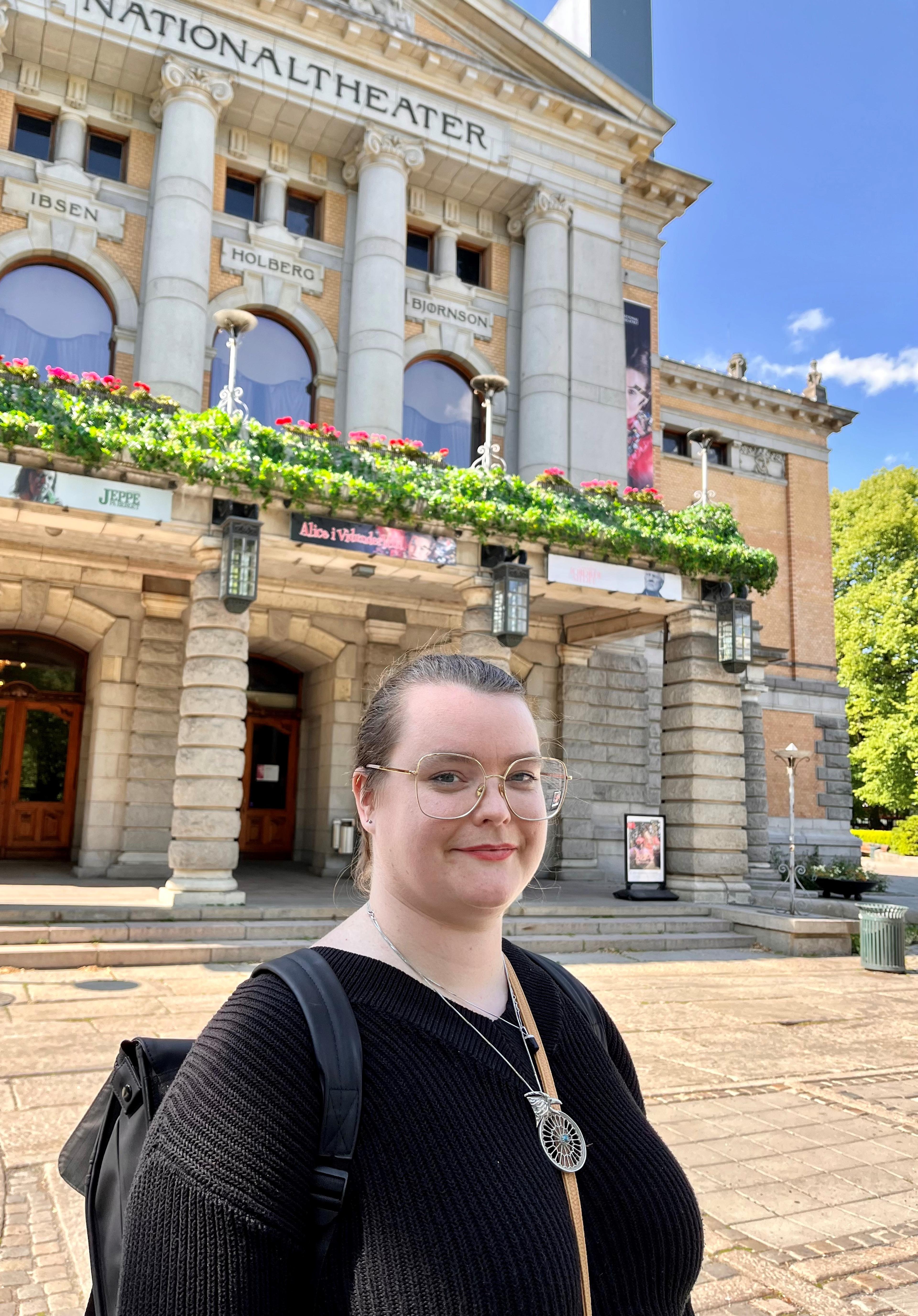 Ivy sitter foran arbeidsbordet sitt på Nationaltheatret, med sysaker i hånden.