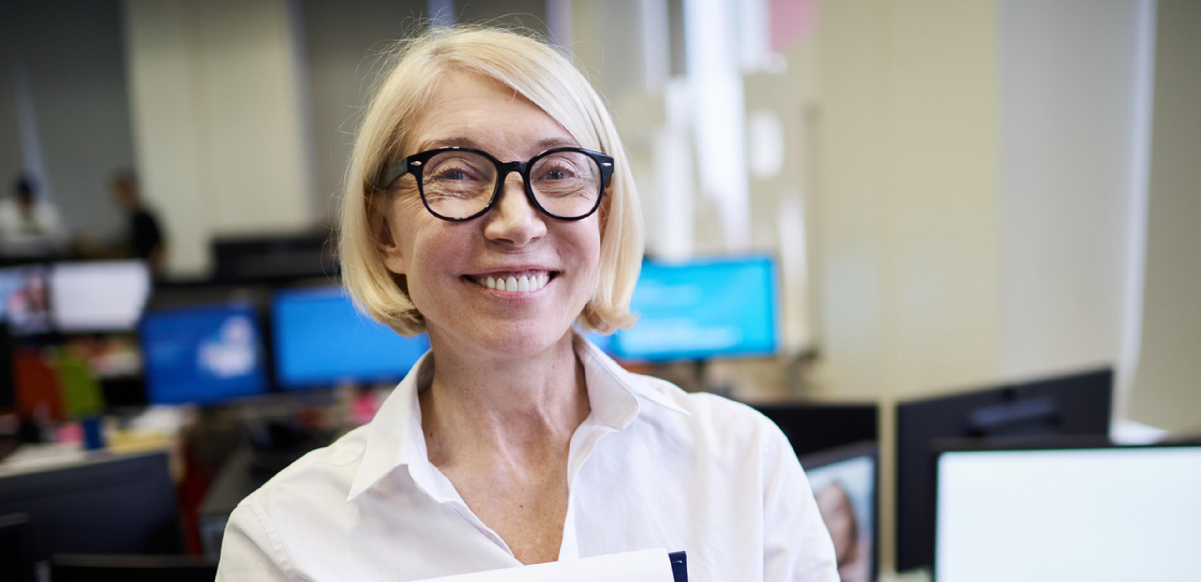 voksen dame, smilenede, i kontorlandskap med en mappe i hånden