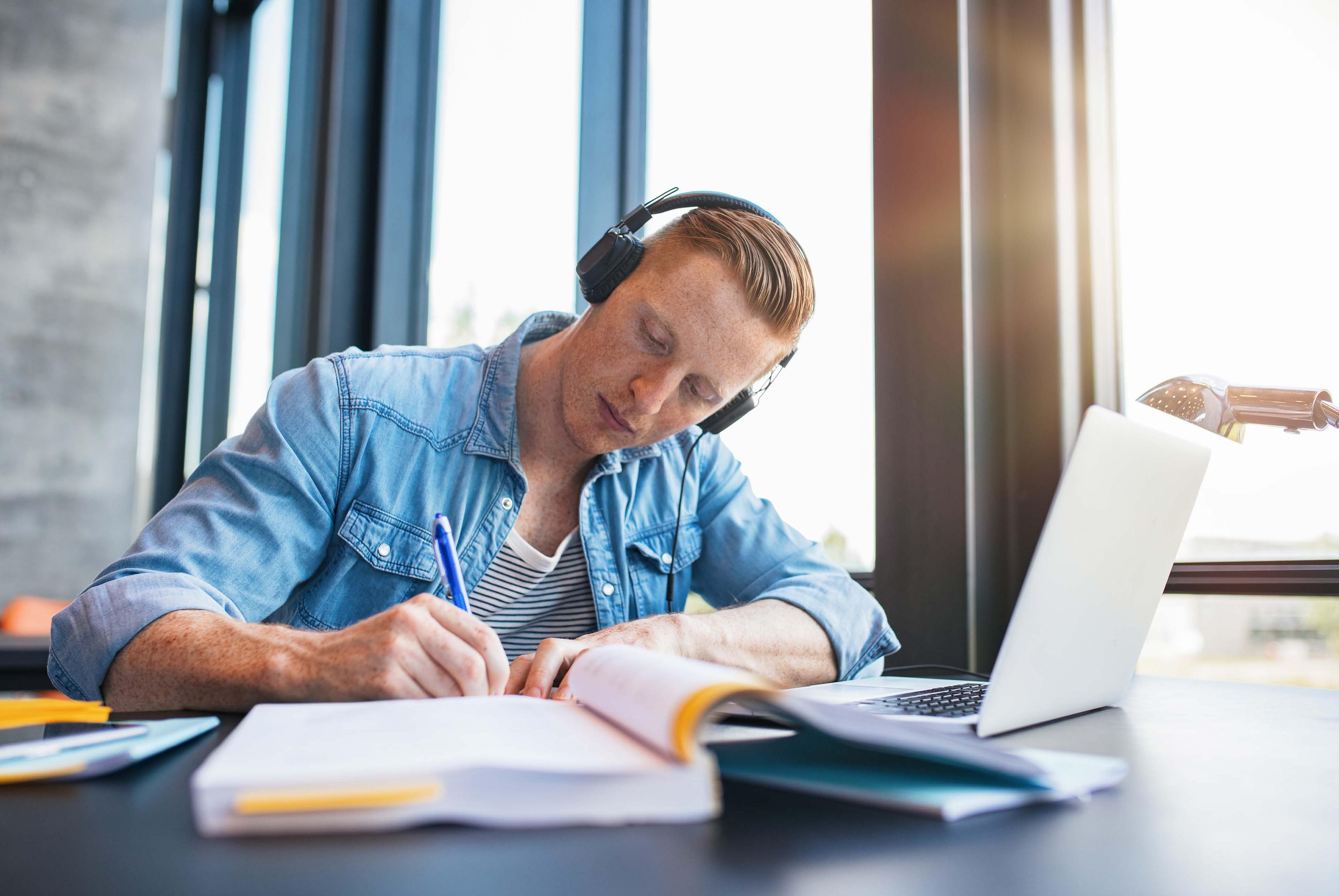 Mann med laptop og headset skriver med penn