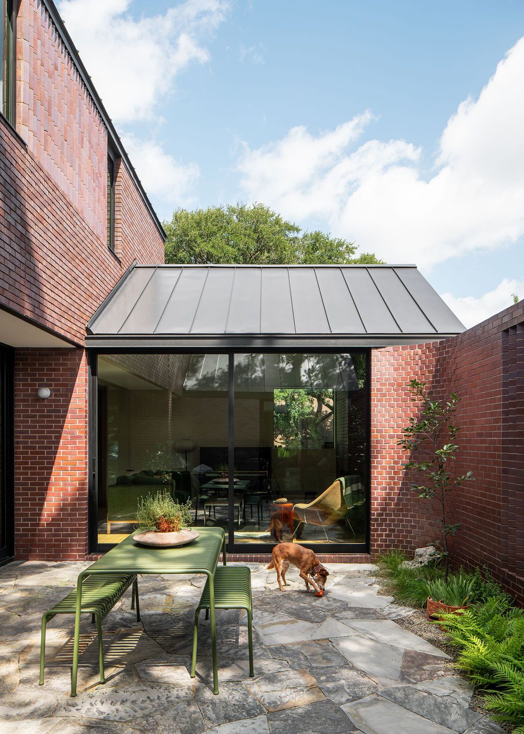 Dog plays beside an outdoor dining table in a brick courtyard