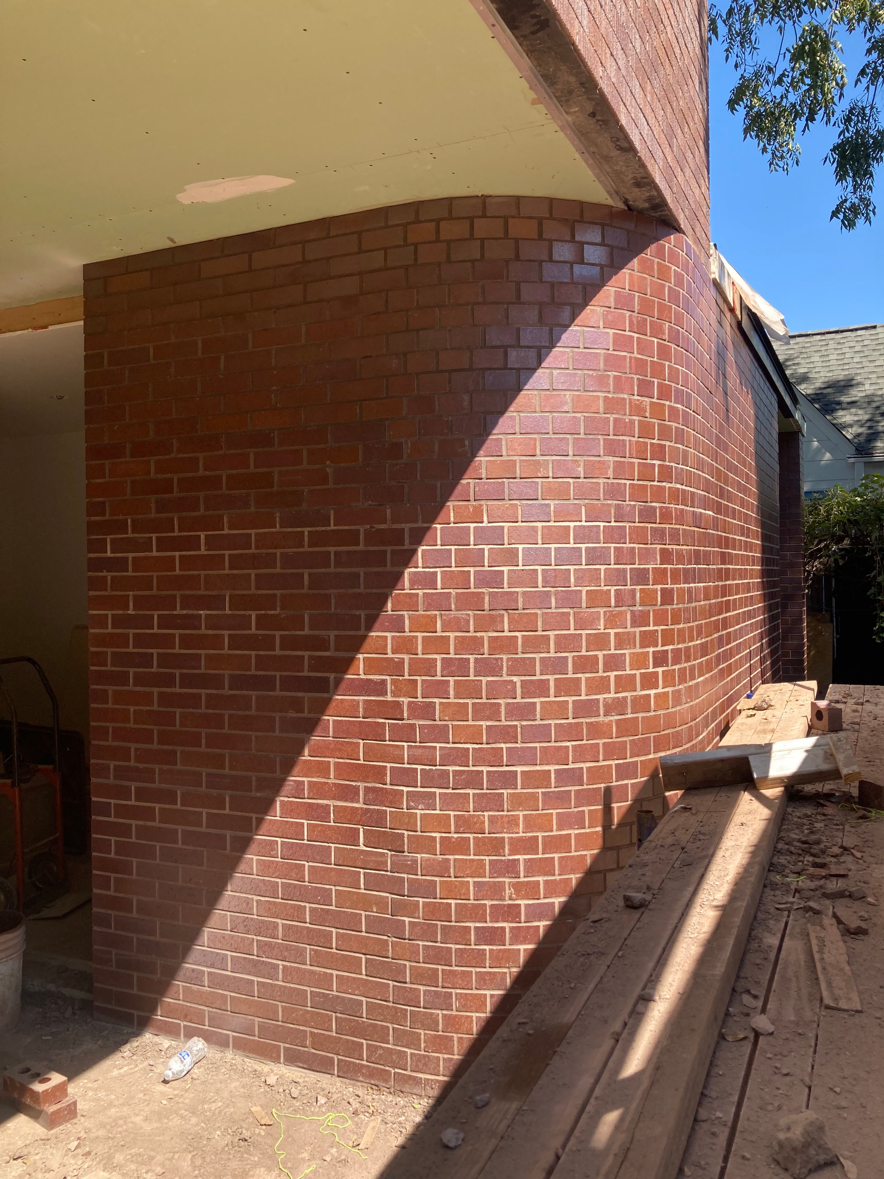 Curved brick wall under construction beside wooden scaffolding