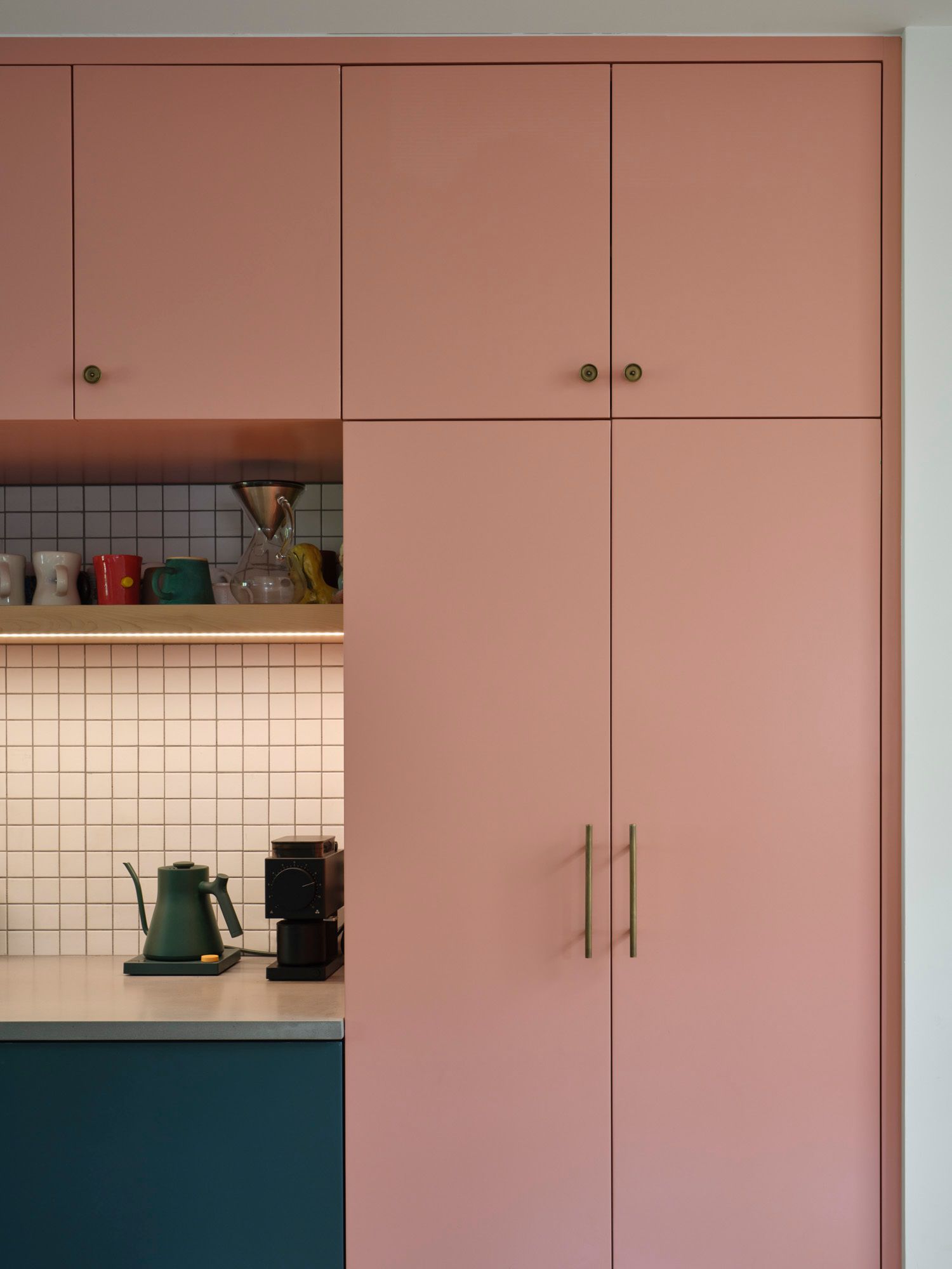 Pink kitchen cabinets beside a counter with kettle and coffee grinder