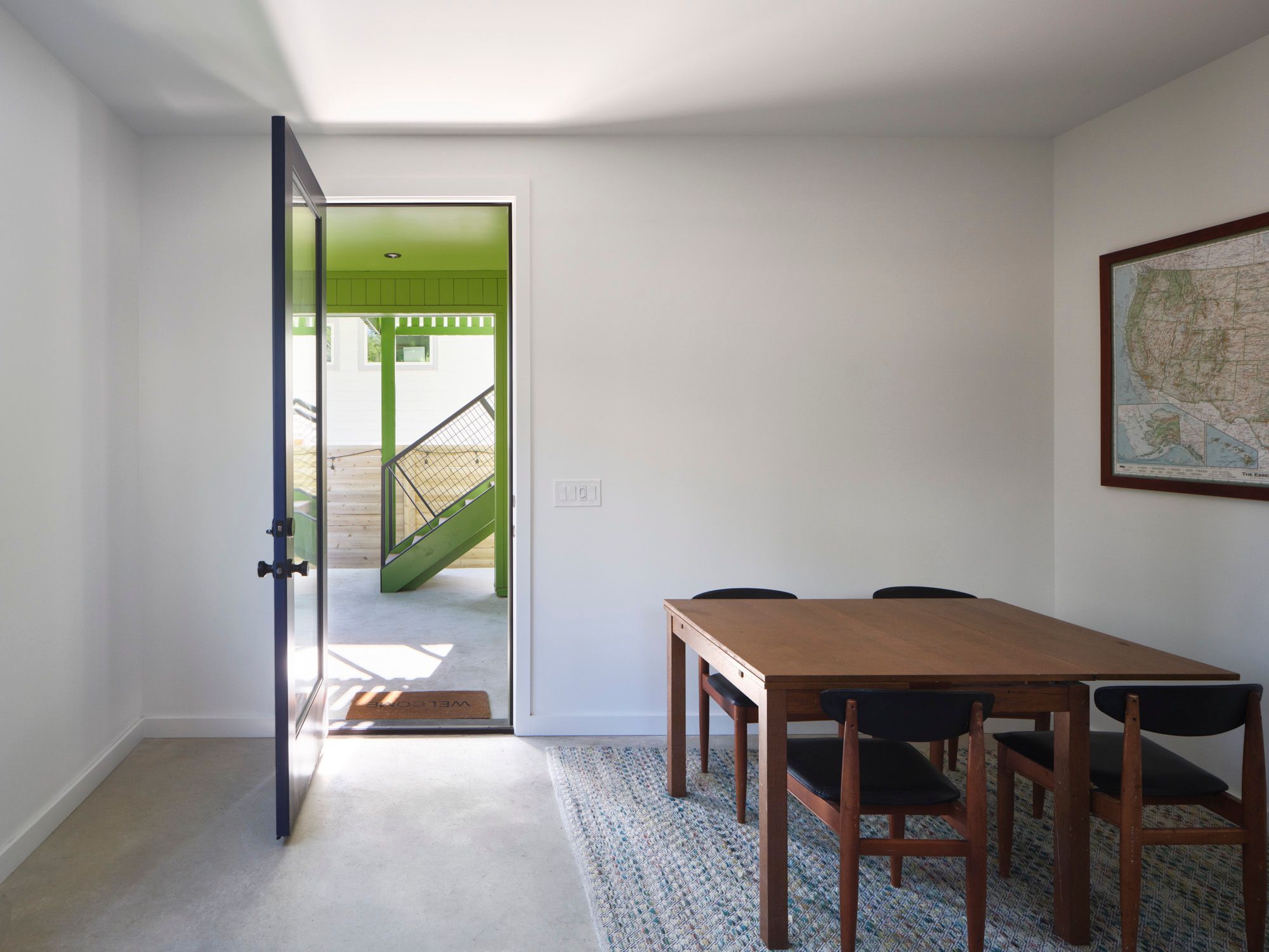 Dining room with wooden table, four chairs, and open exterior door
