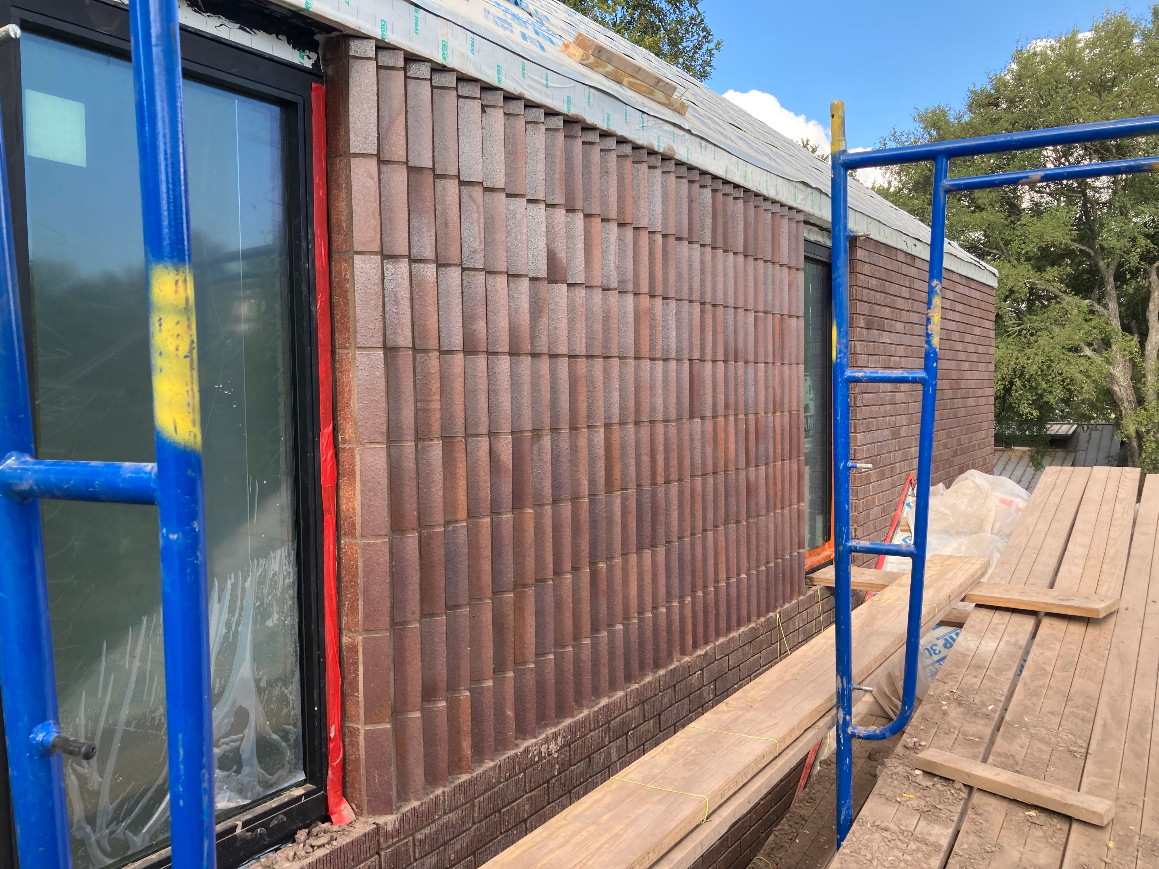 Scaffolding surrounds a building under construction with newly installed brick siding
