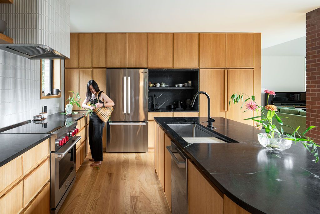 Woman arranges flowers in a wood-paneled kitchen with black countertops