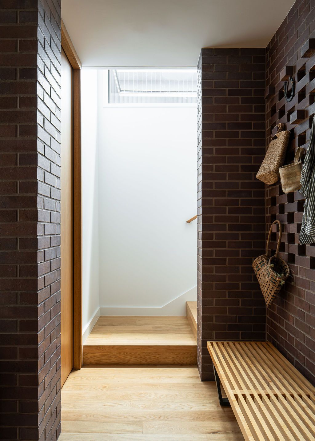 Brick entryway with wooden bench, hanging baskets and skylit stairs