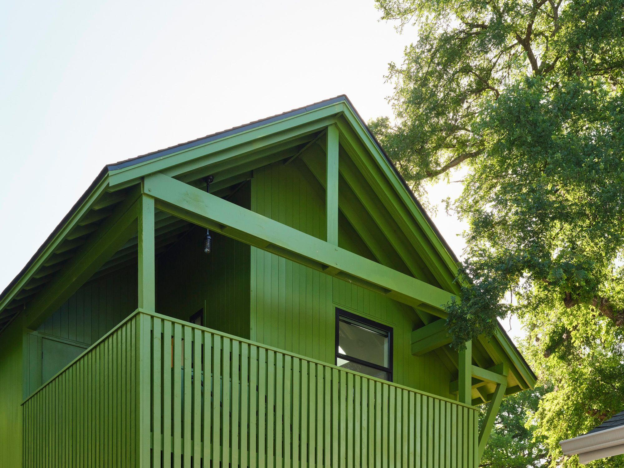 Green house with an upper-level balcony beside a large tree