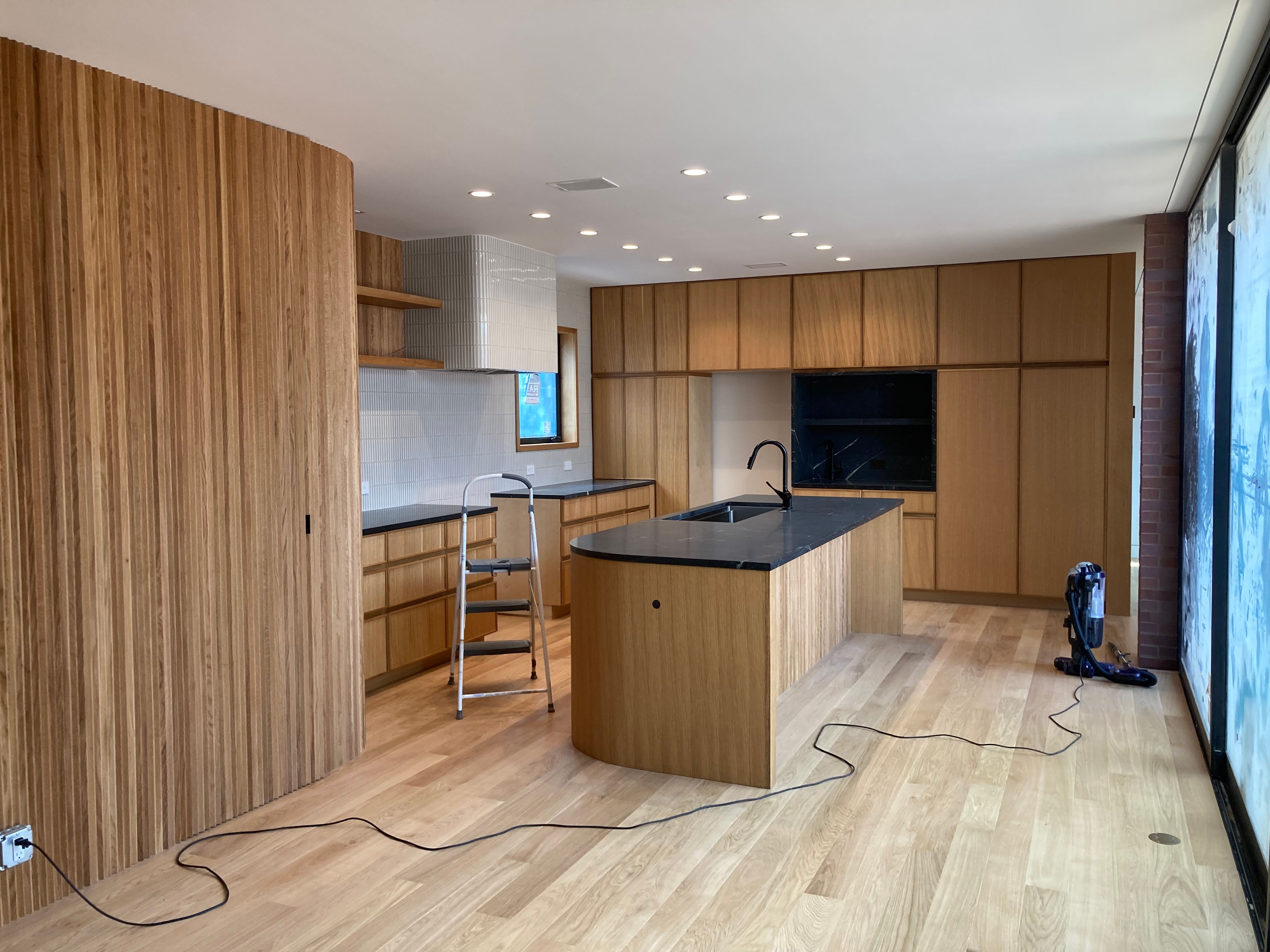 Kitchen under construction with wood cabinetry, island, stepladder and vacuum