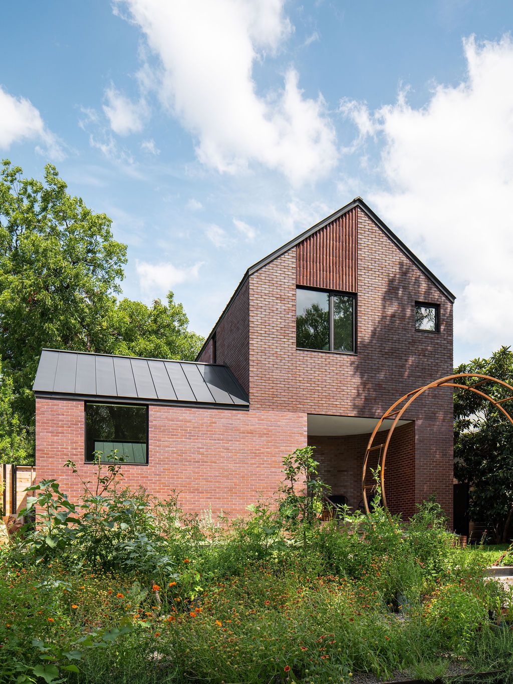 Brick house with gabled roof overlooking a densely planted courtyard