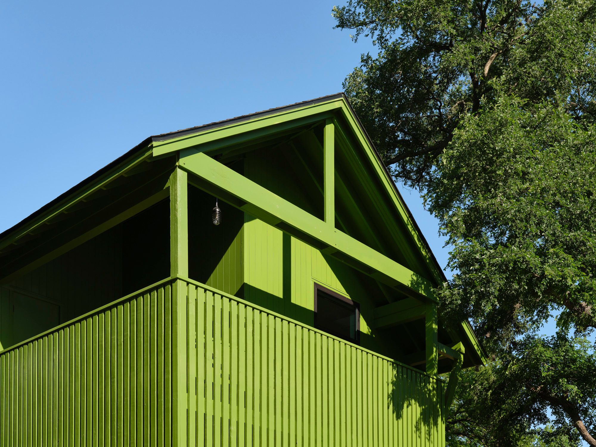 Green timber house with a gabled roof beside mature trees