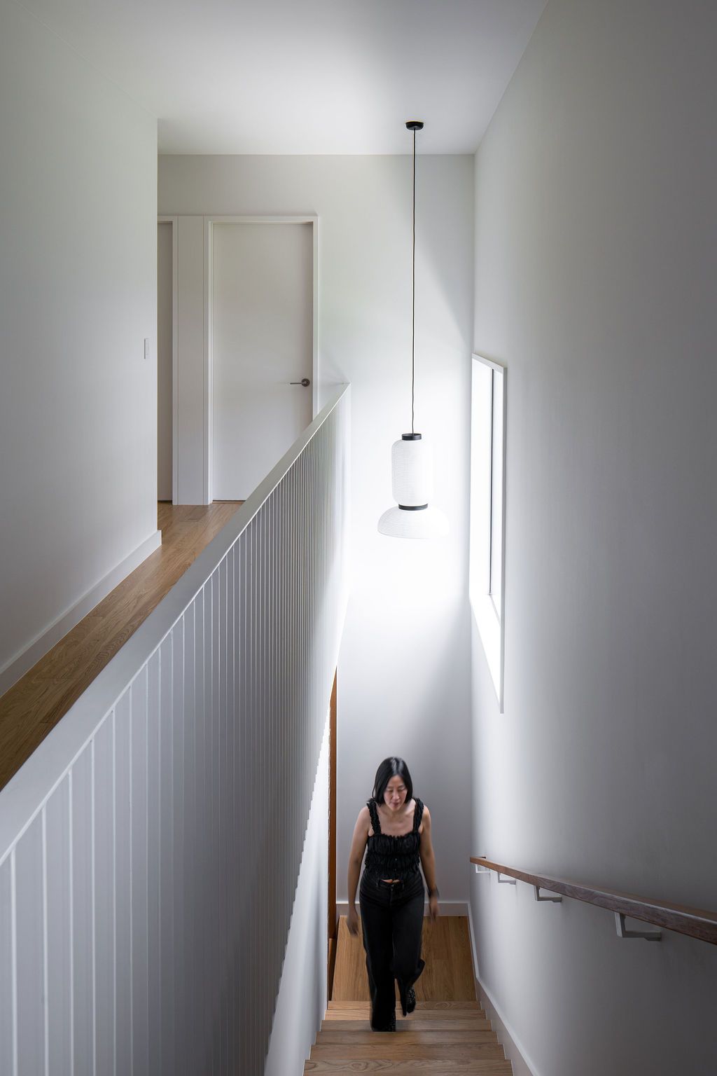 Woman climbs a wooden staircase beneath pendant lights