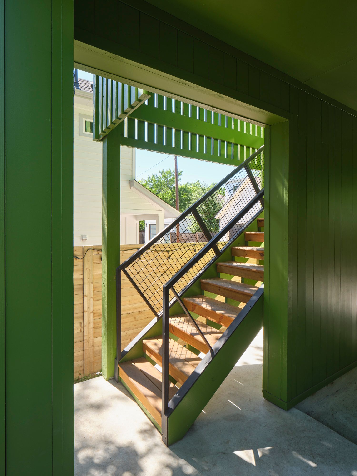 Wooden outdoor staircase with metal mesh railings beside green siding