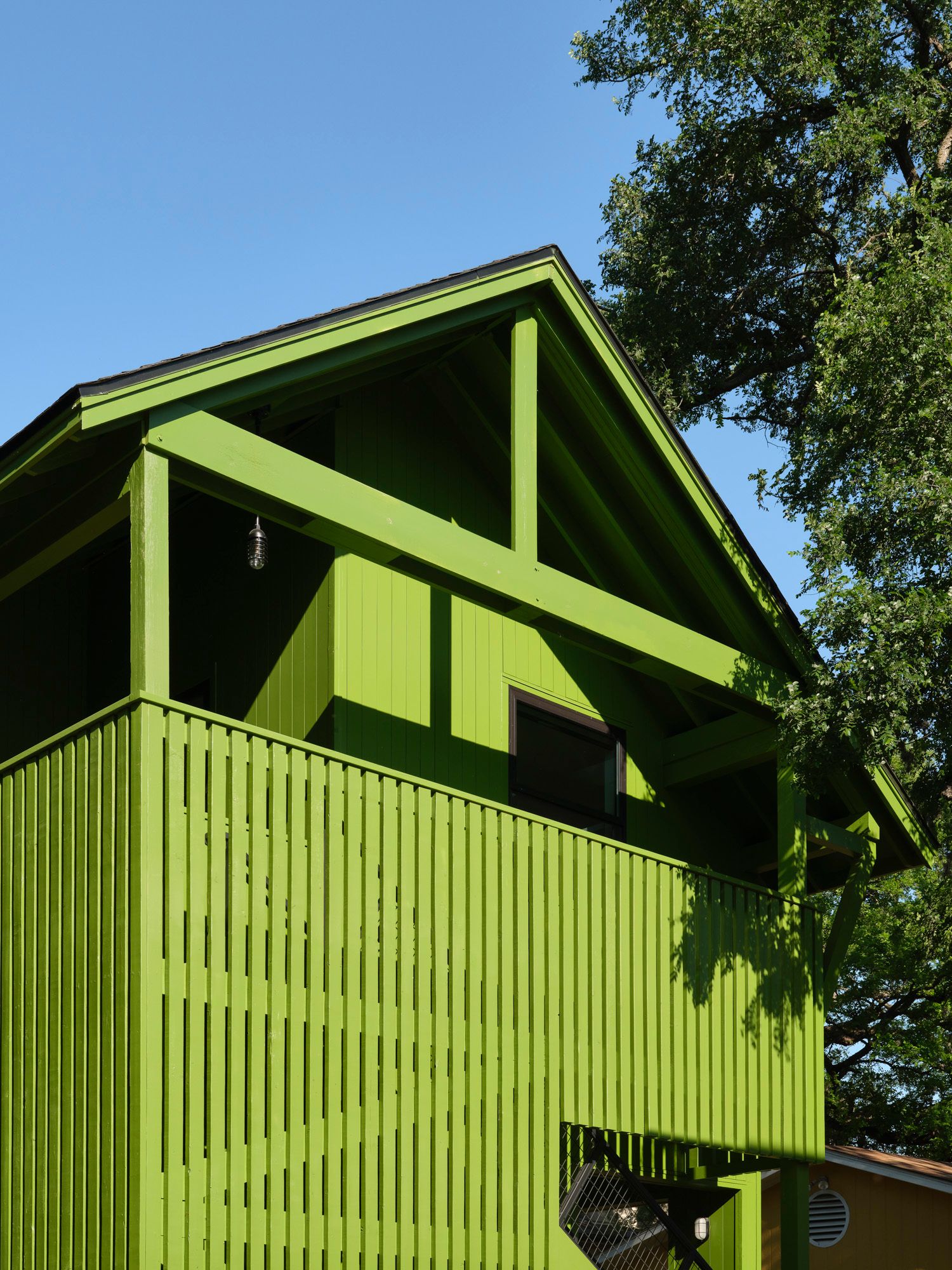 Bright green wooden house with screened balcony beneath mature trees
