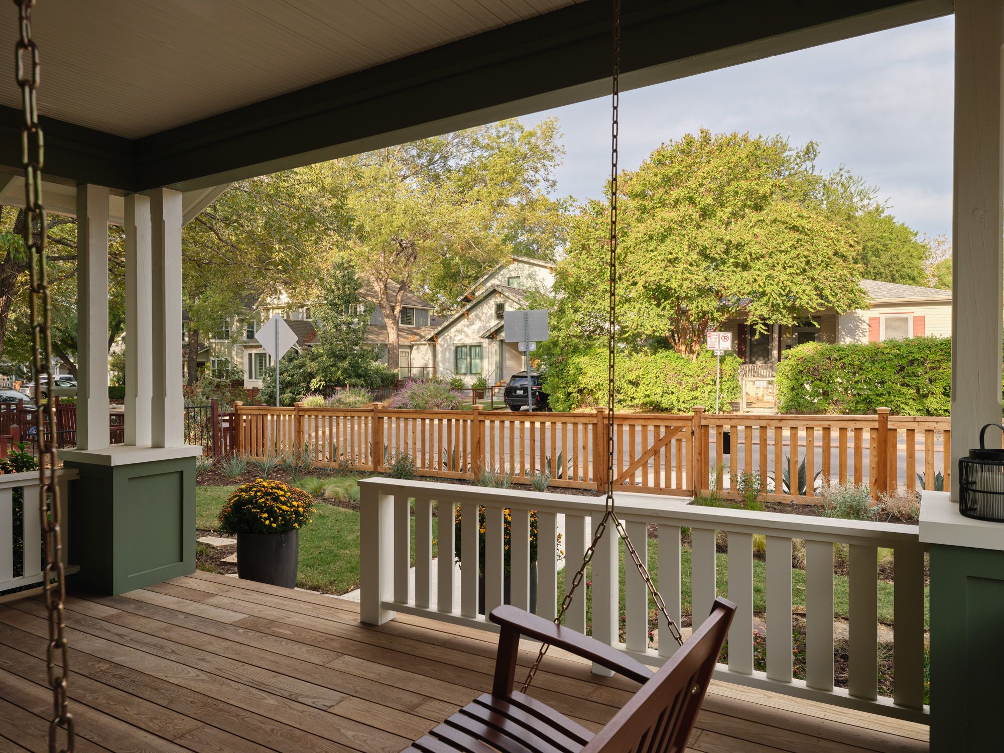 Porch swing overlooks a fenced garden and residential street