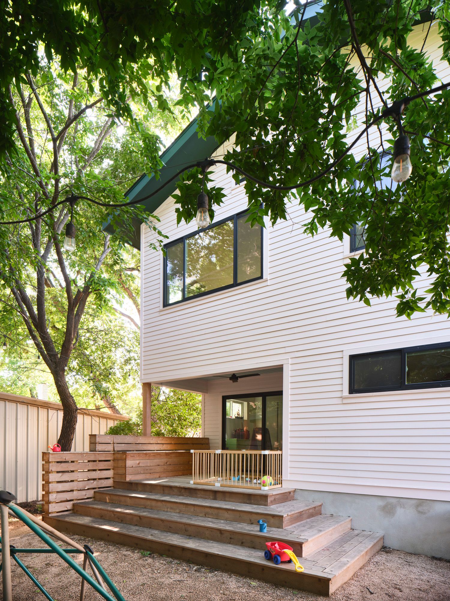 Modern house with tiered wooden deck and children's toys under trees