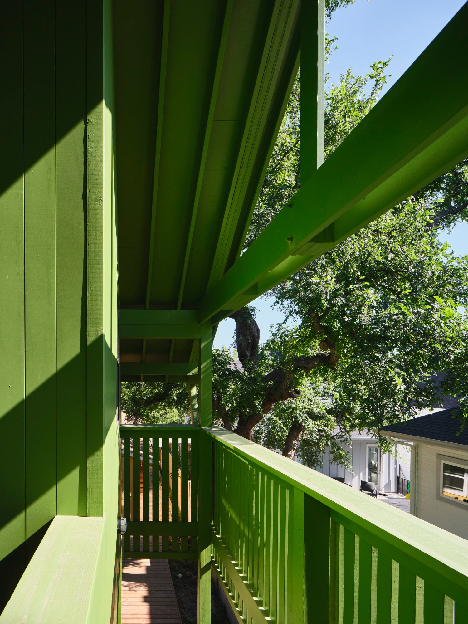 Green wooden balcony walkway overlooking trees and neighboring houses
