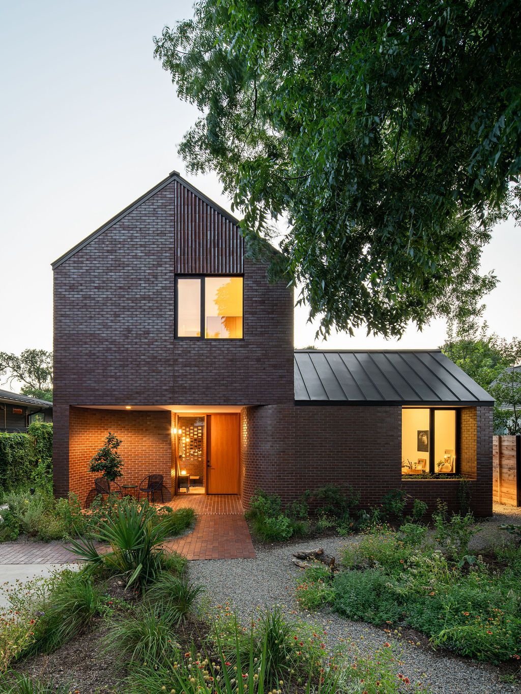Brick house with illuminated windows overlooking a planted courtyard