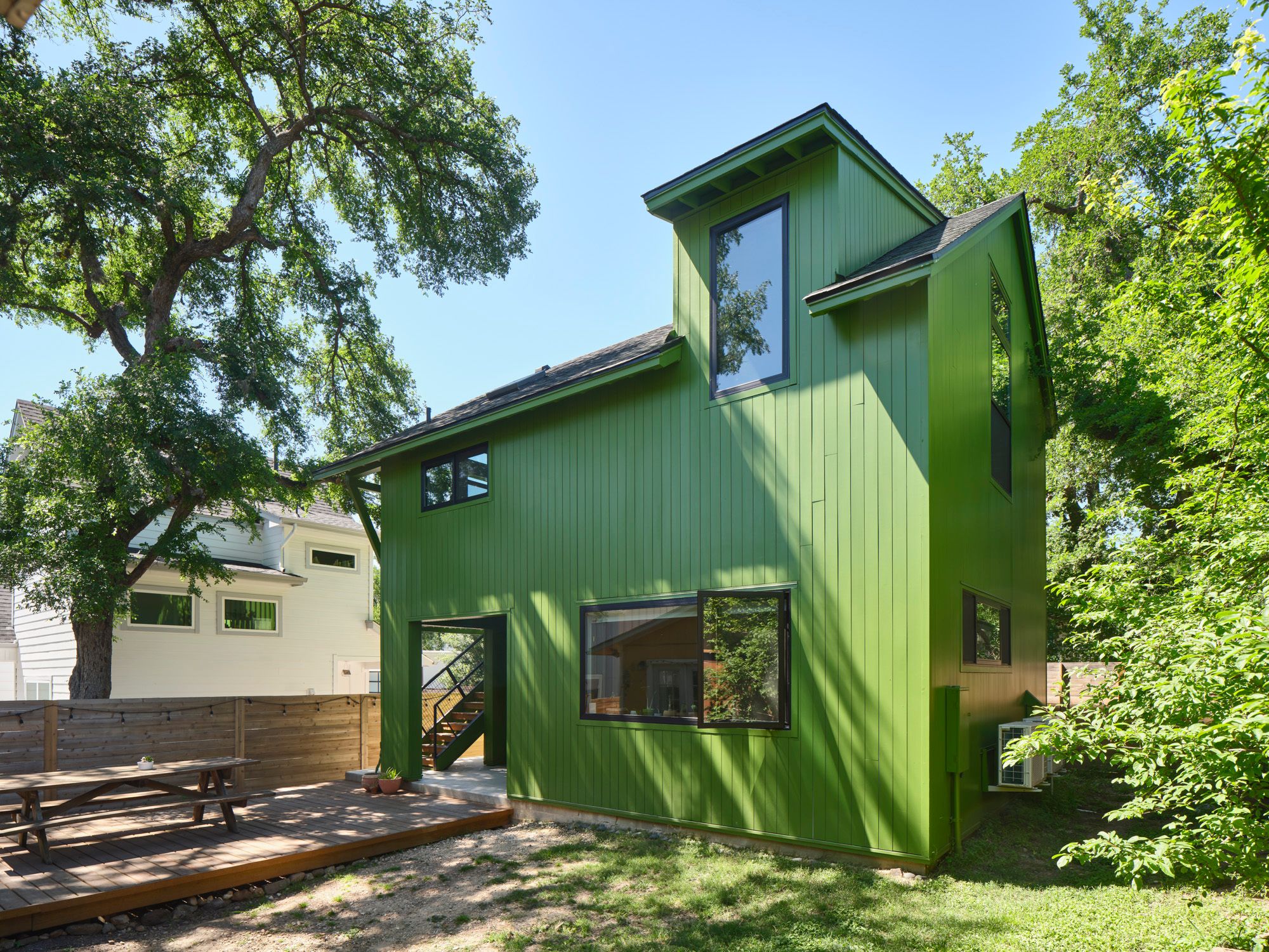 Green two-story house with large windows and a wooden deck