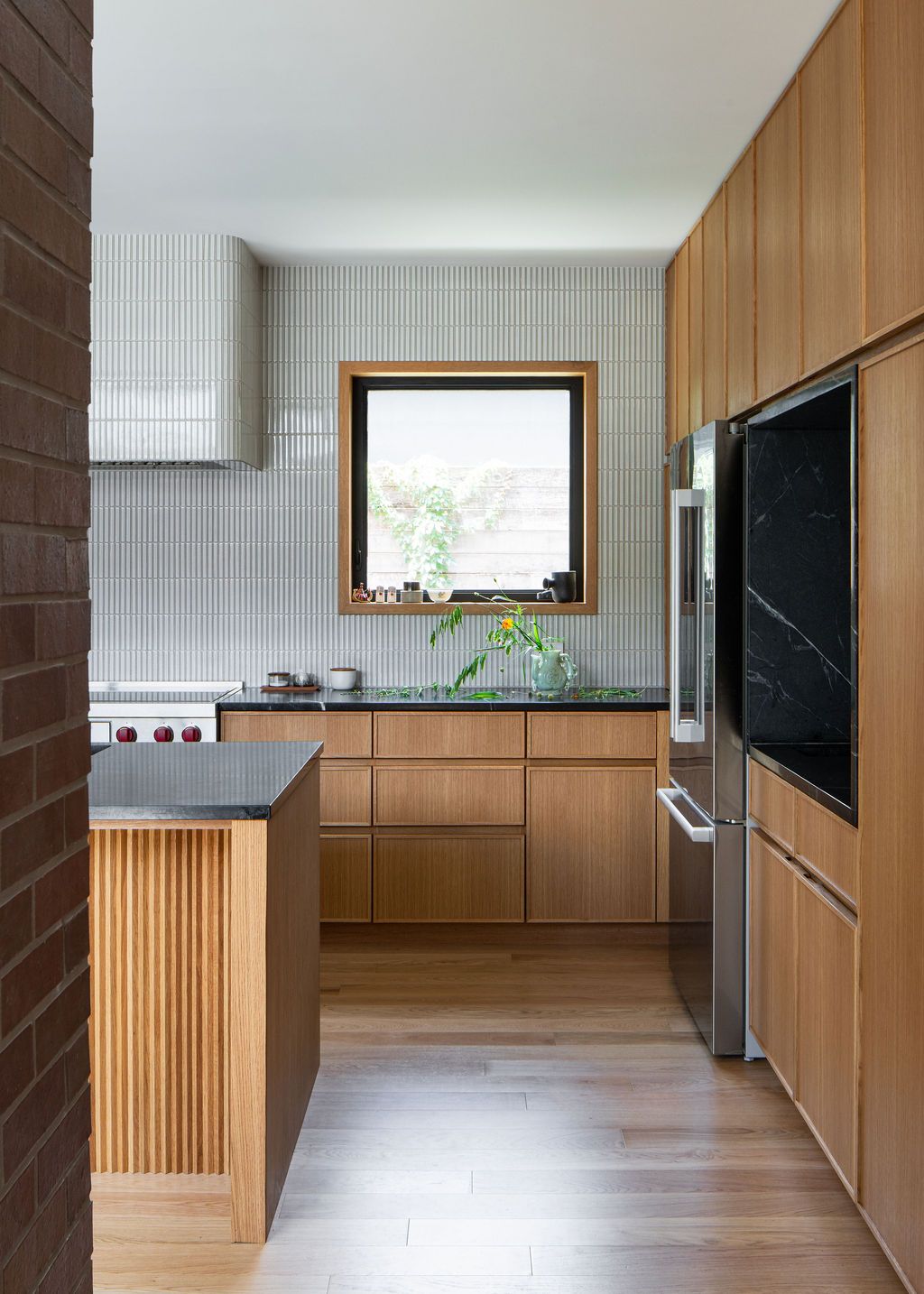 Kitchen with wood cabinetry, tiled walls, island and courtyard-facing window