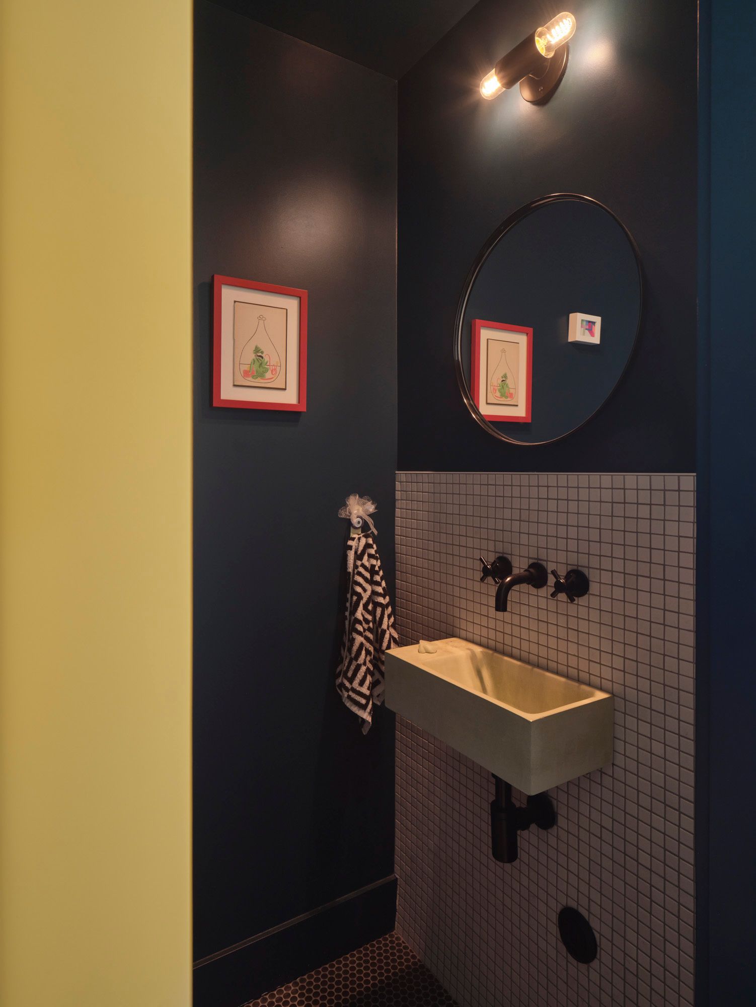 Compact bathroom with wall-mounted sink, round mirror and framed artwork
