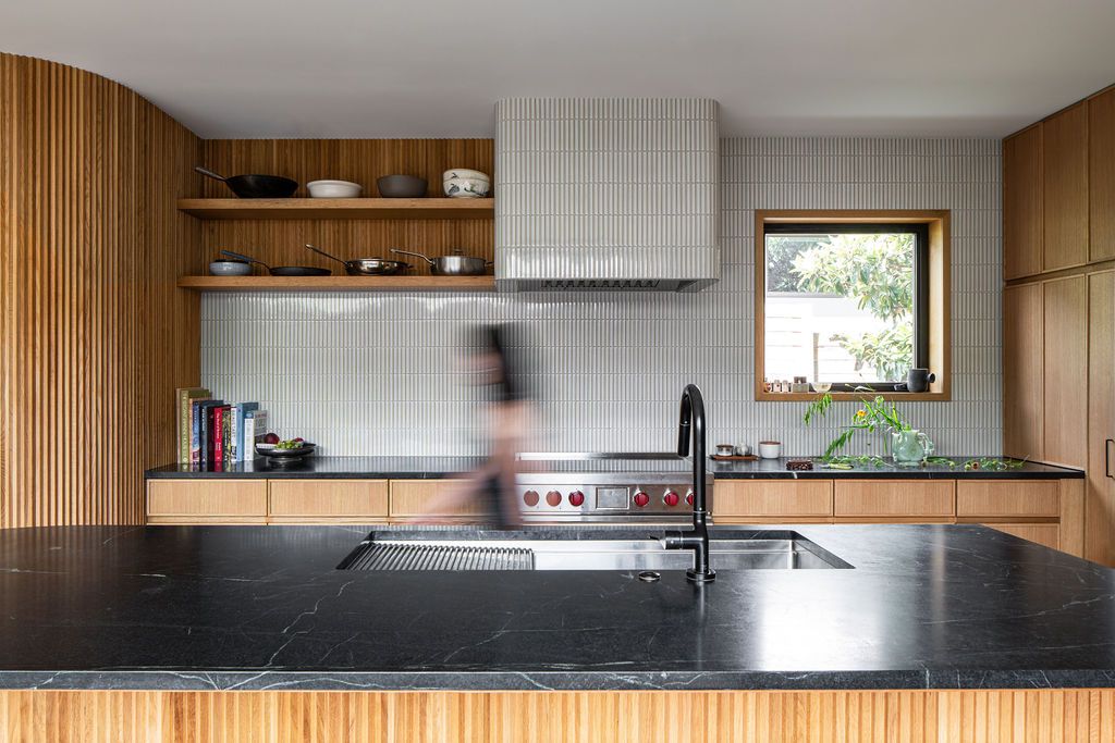 Person walks through a wood-paneled kitchen with black stone island