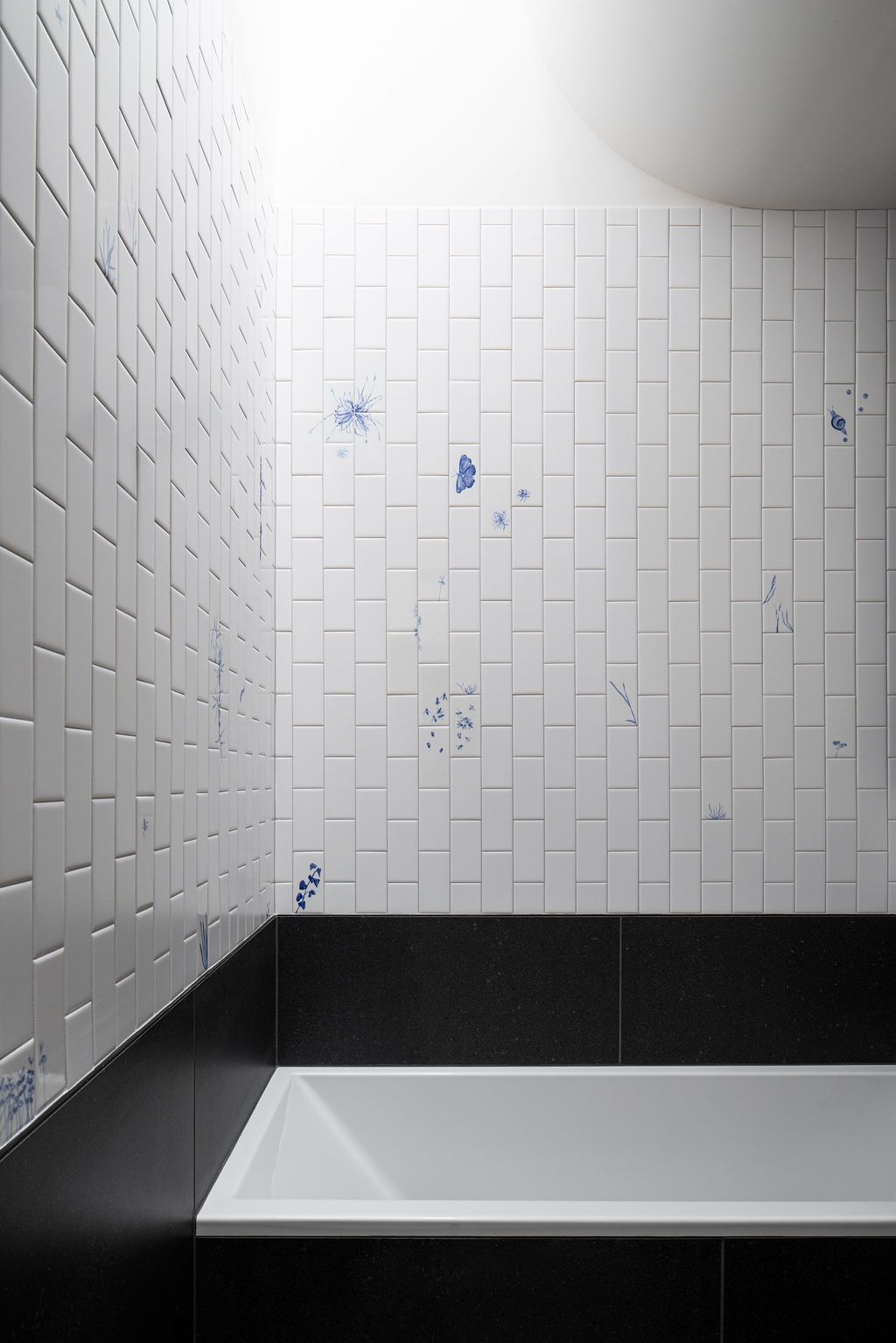 Bathtub beneath white tiled walls with scattered blue botanical illustrations
