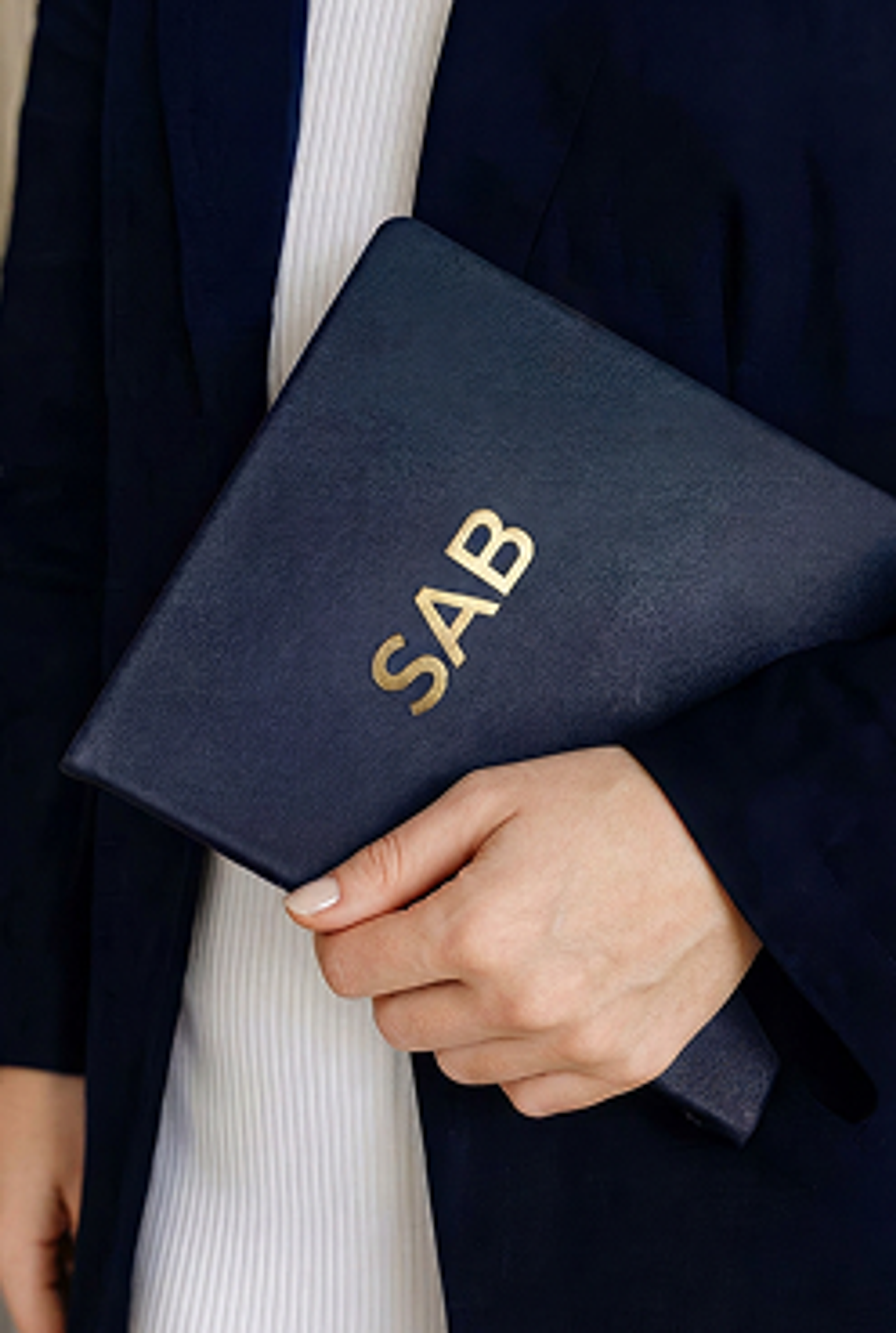 A person holding a dark blue portfolio folder with gold embossed letters spelling SAB