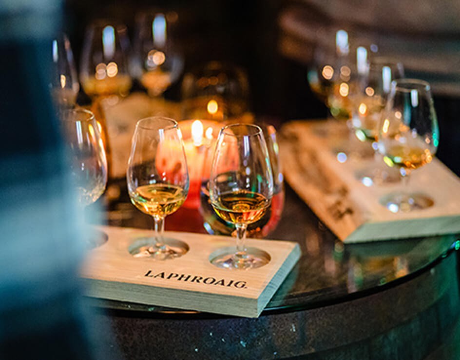 Tasting glasses filled with amber whisky resting on branded wooden Laphroaig flight board