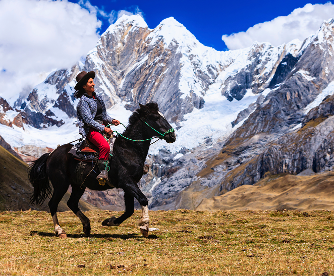 Horse rider crossing a grassy hillside beneath snow-covered Andean peaks.