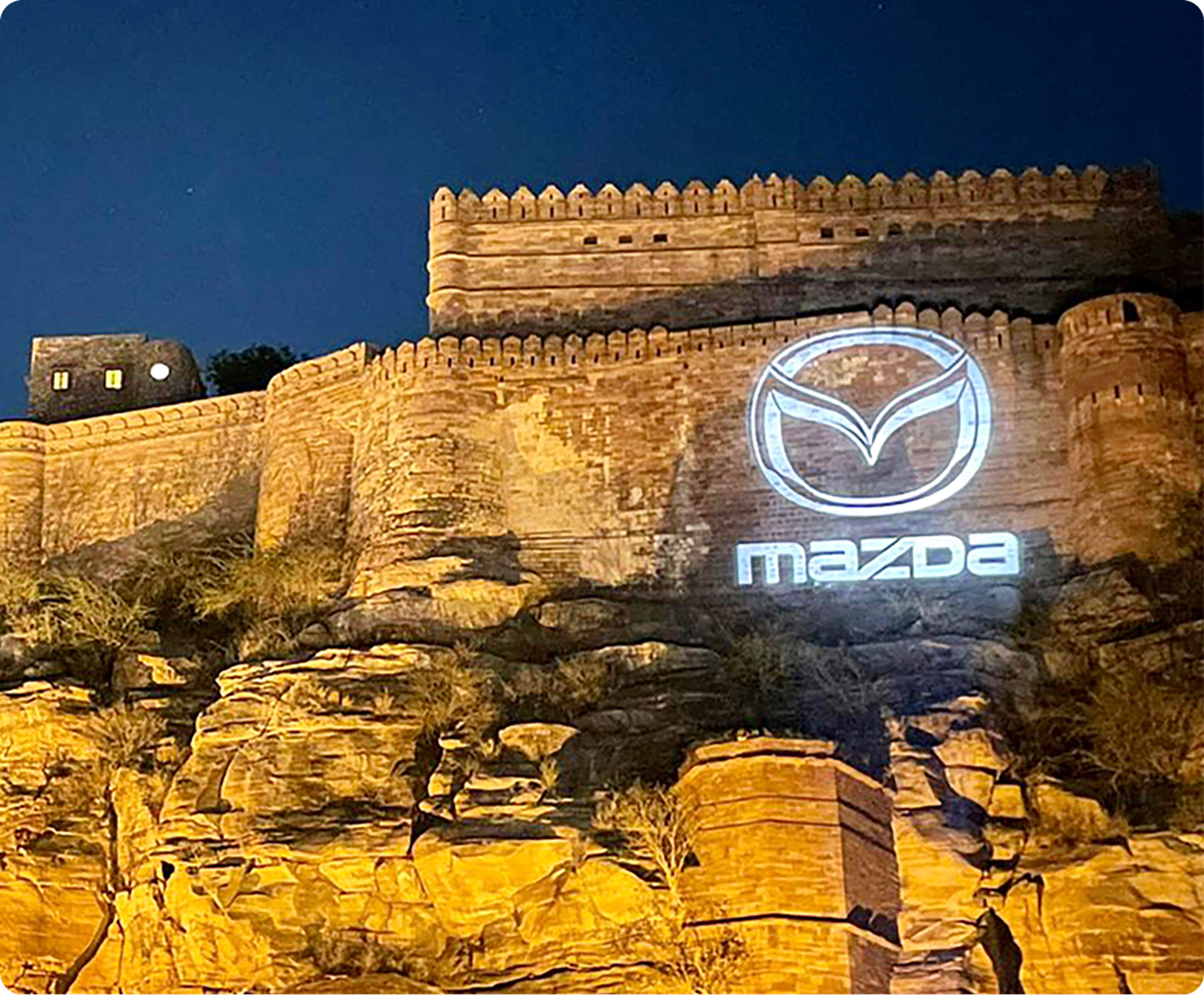 Mazda logo projected onto illuminated fort walls at night.