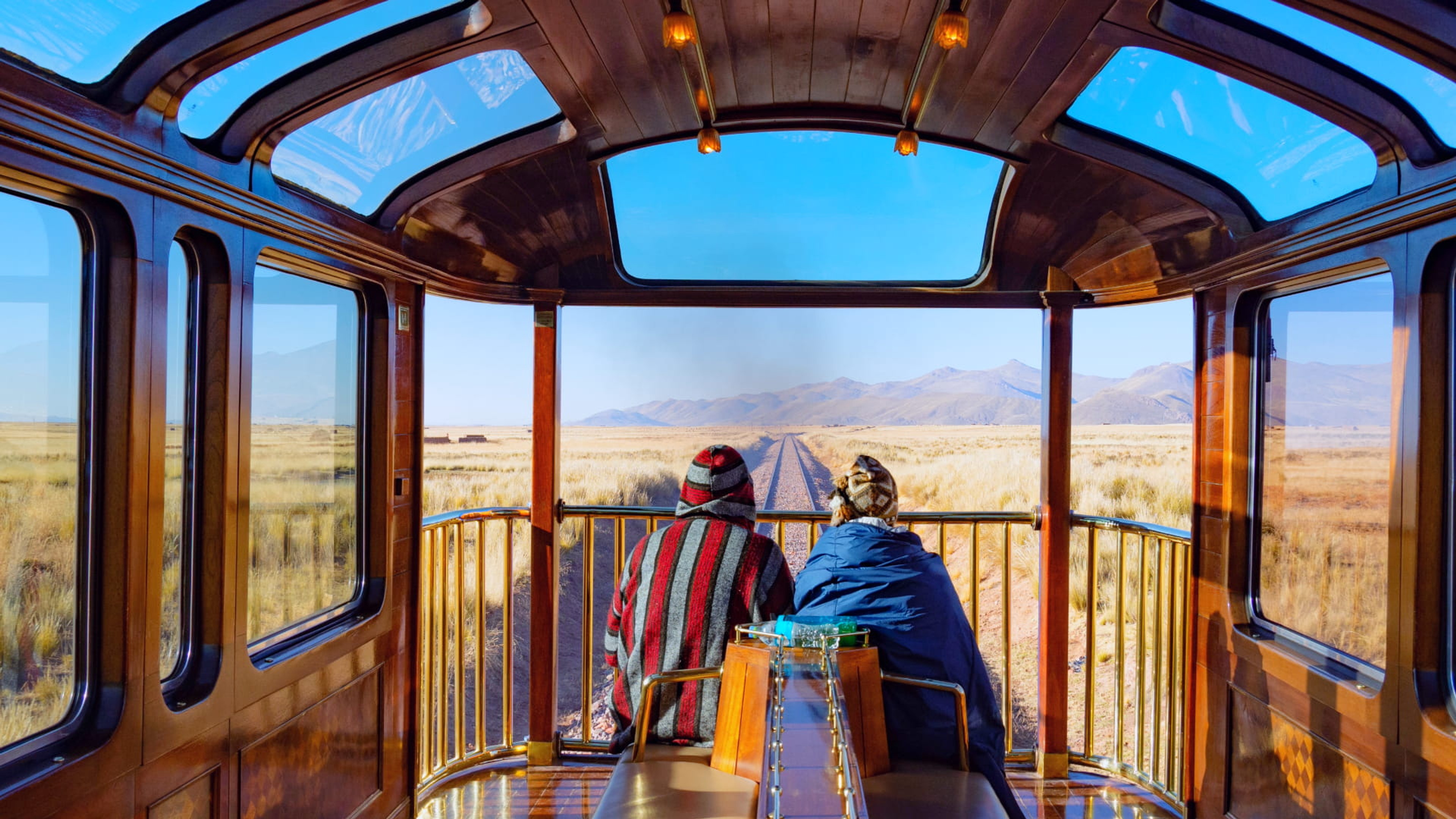 Two passengers enjoying mountain views from a panoramic train carriage in Peru.