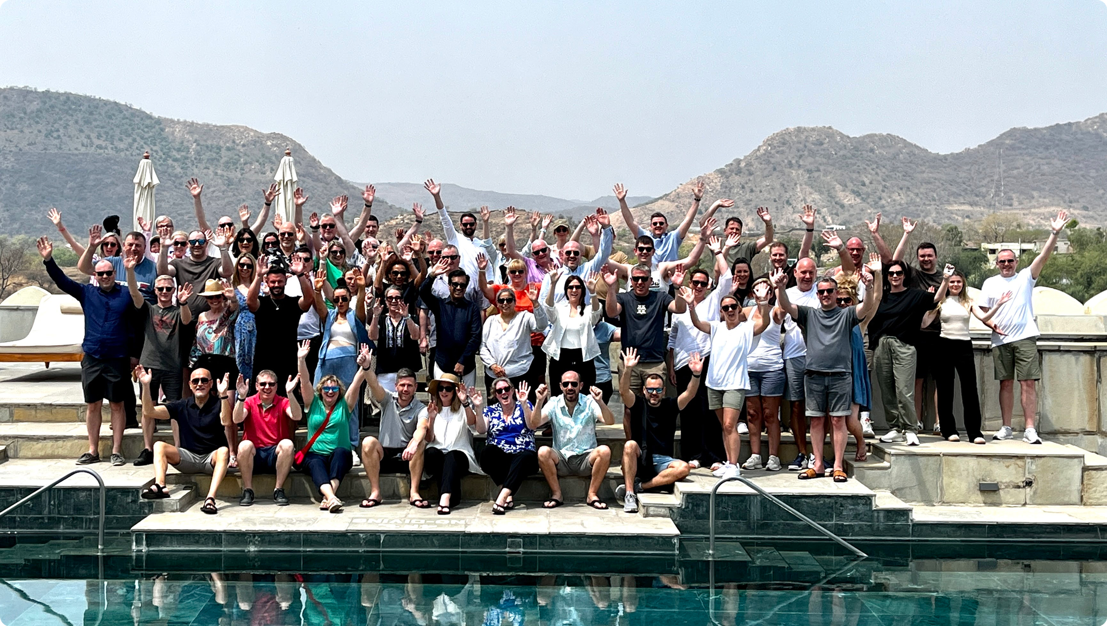 Mazda Elite Club guests waving beside a pool, with mountains in the background.