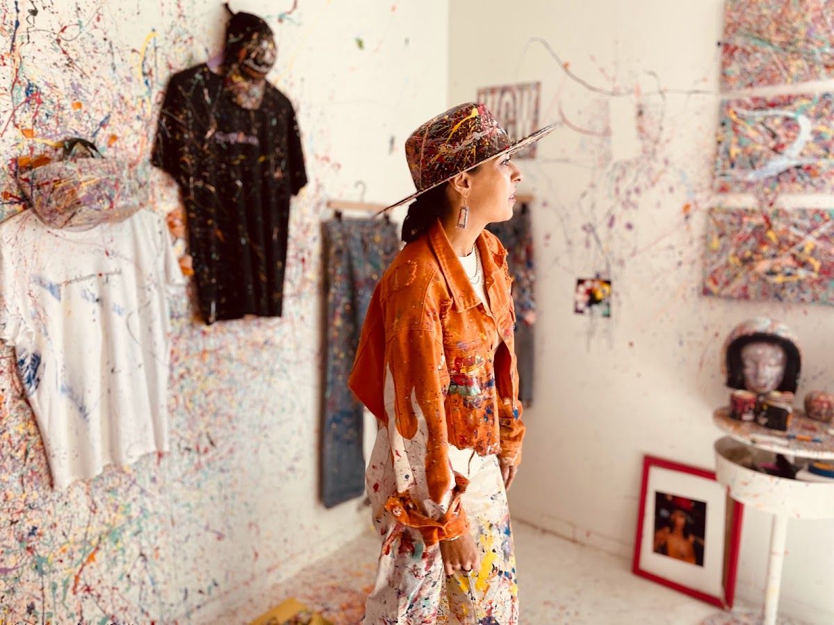 artists in a room covered in multicoloured splatter paint with paint all over her clothes 