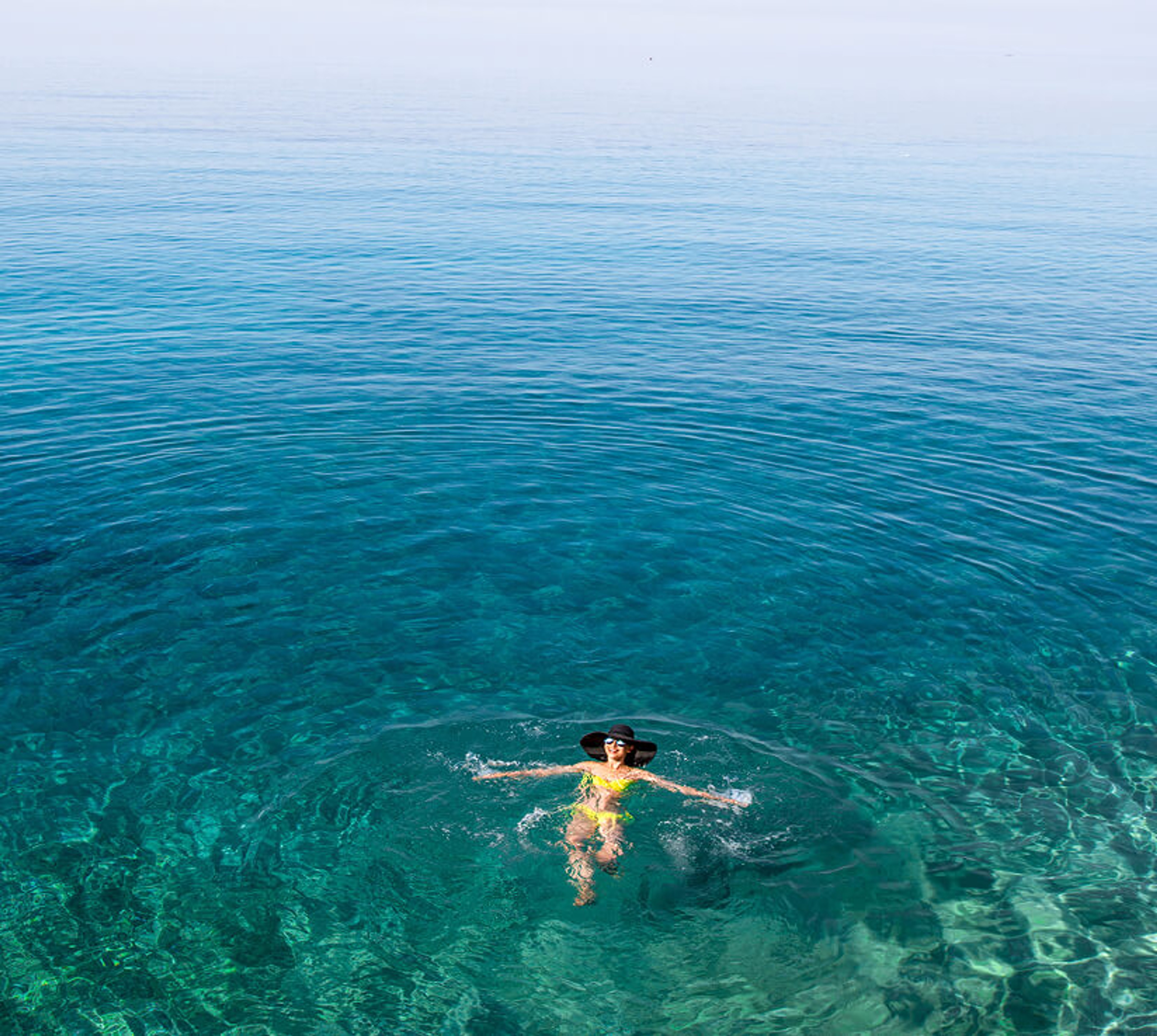 High-angle view of a person wearing a yellow swimsuit floating in clear turquoise sea water.
