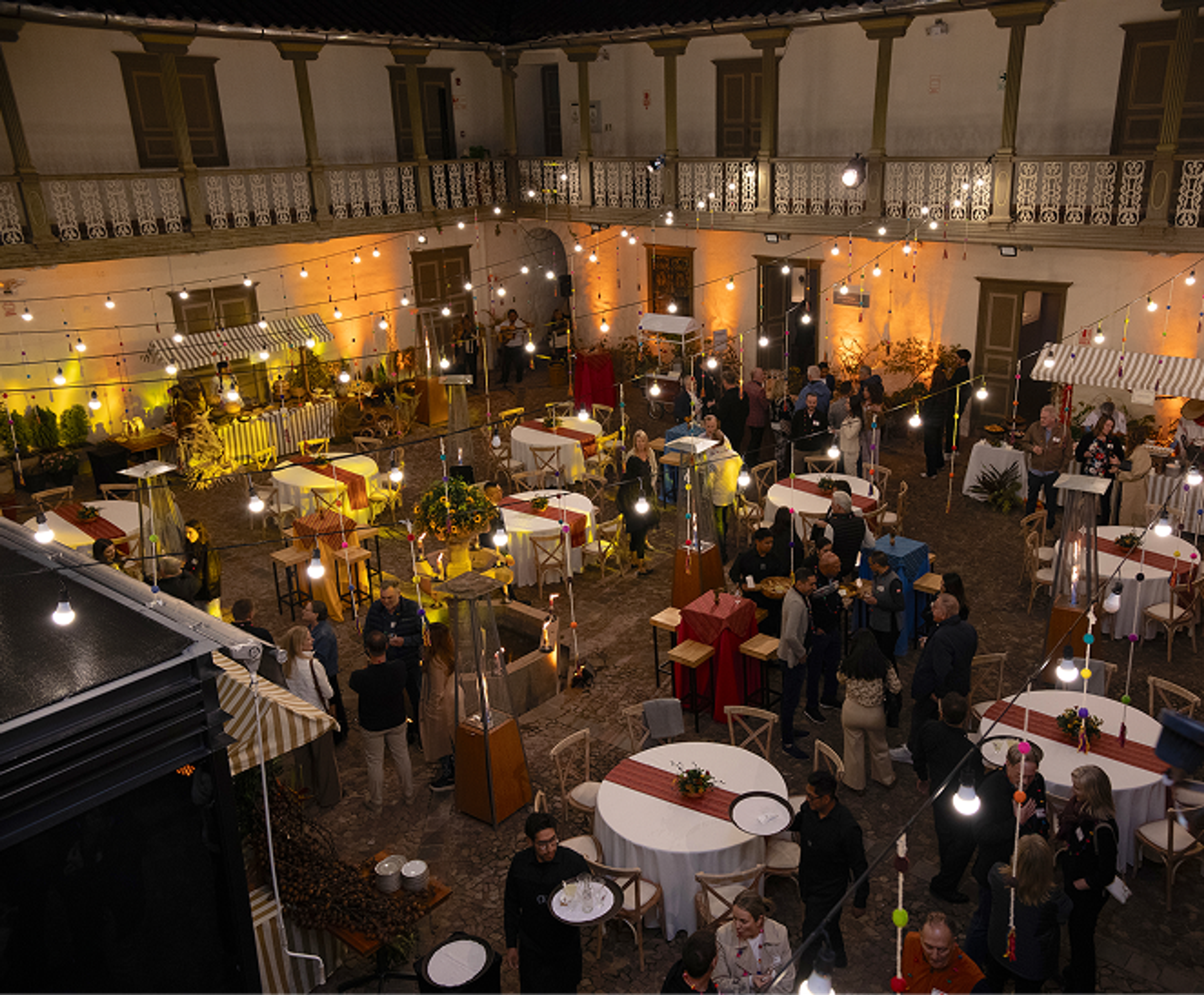 Guests gathering around tables and food stalls beneath festoon lights at an evening courtyard reception.