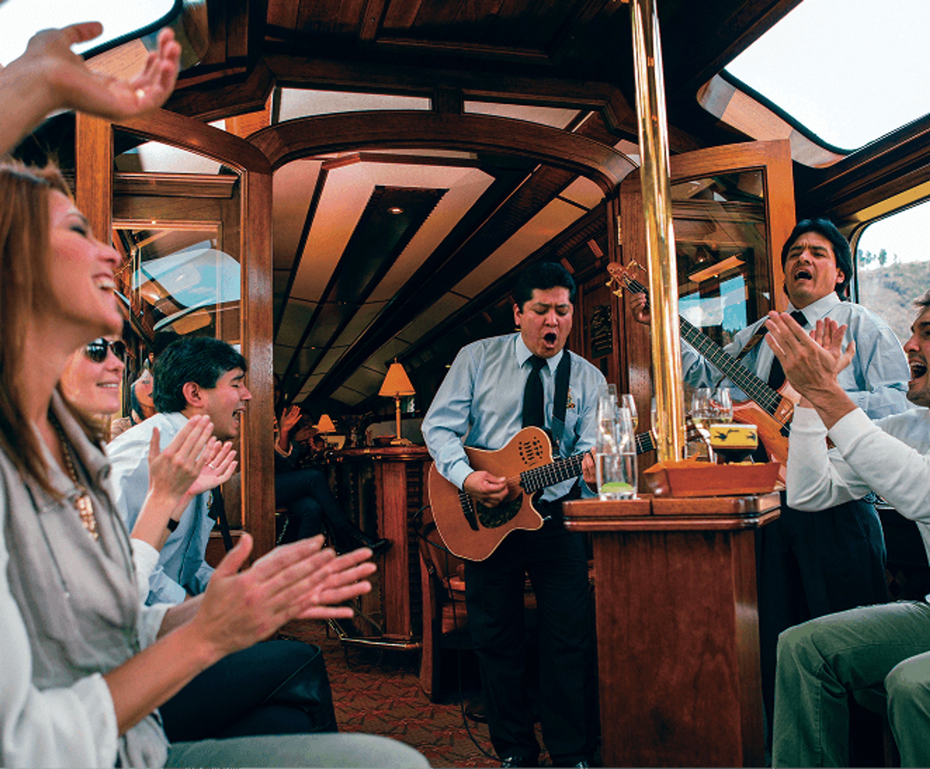 Passengers clapping along to live guitar music inside a wood-panelled train carriage.Passengers clapping along to live guitar music inside a wood-panelled train carriage.