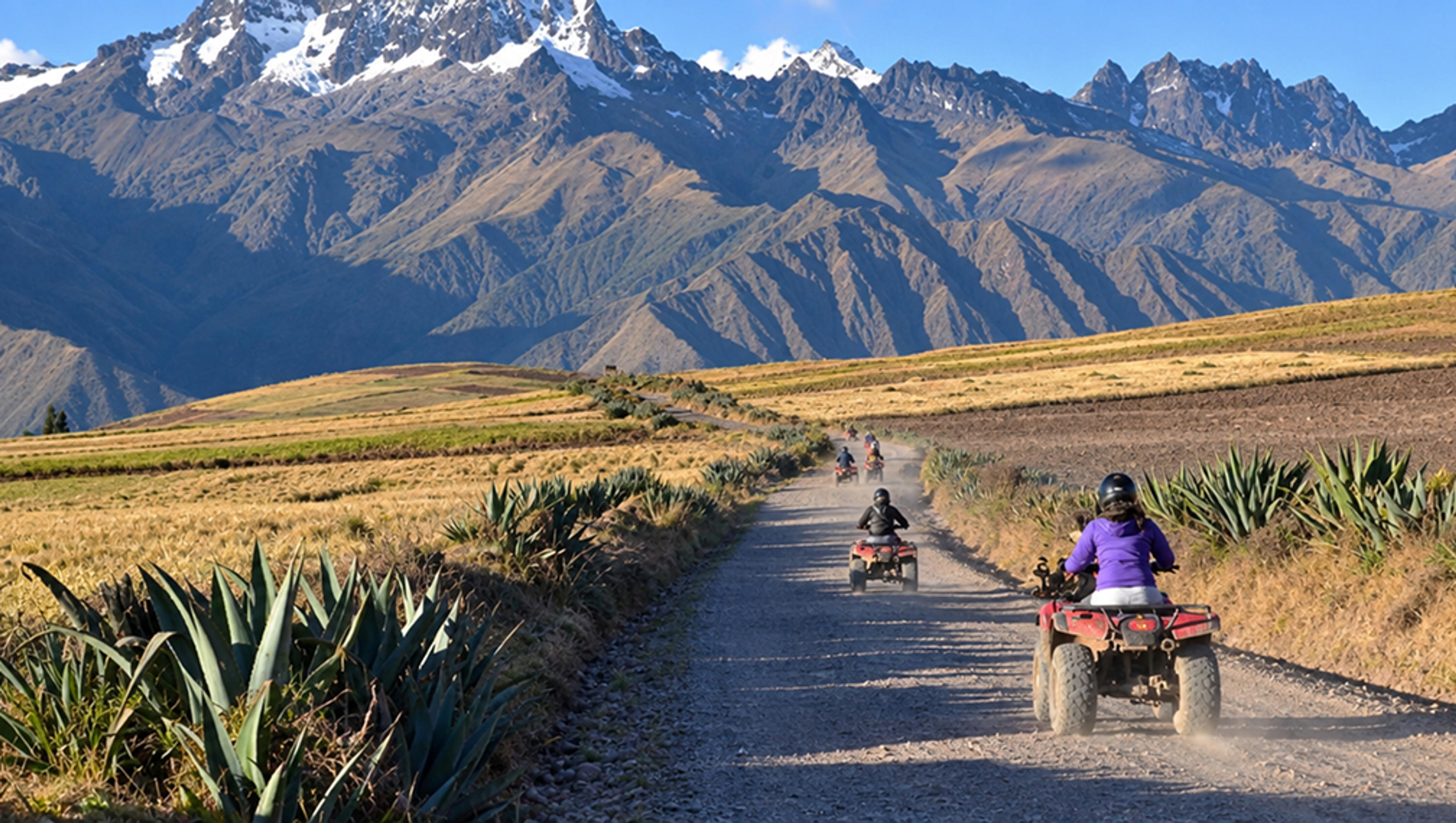 Quad bikers following a dusty track through farmland beneath the Andes.