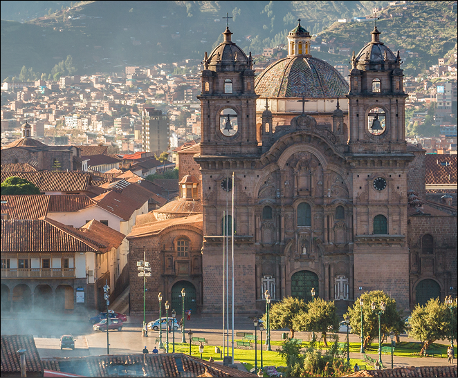 Ornate church overlooking a square, with hillside buildings in the background.