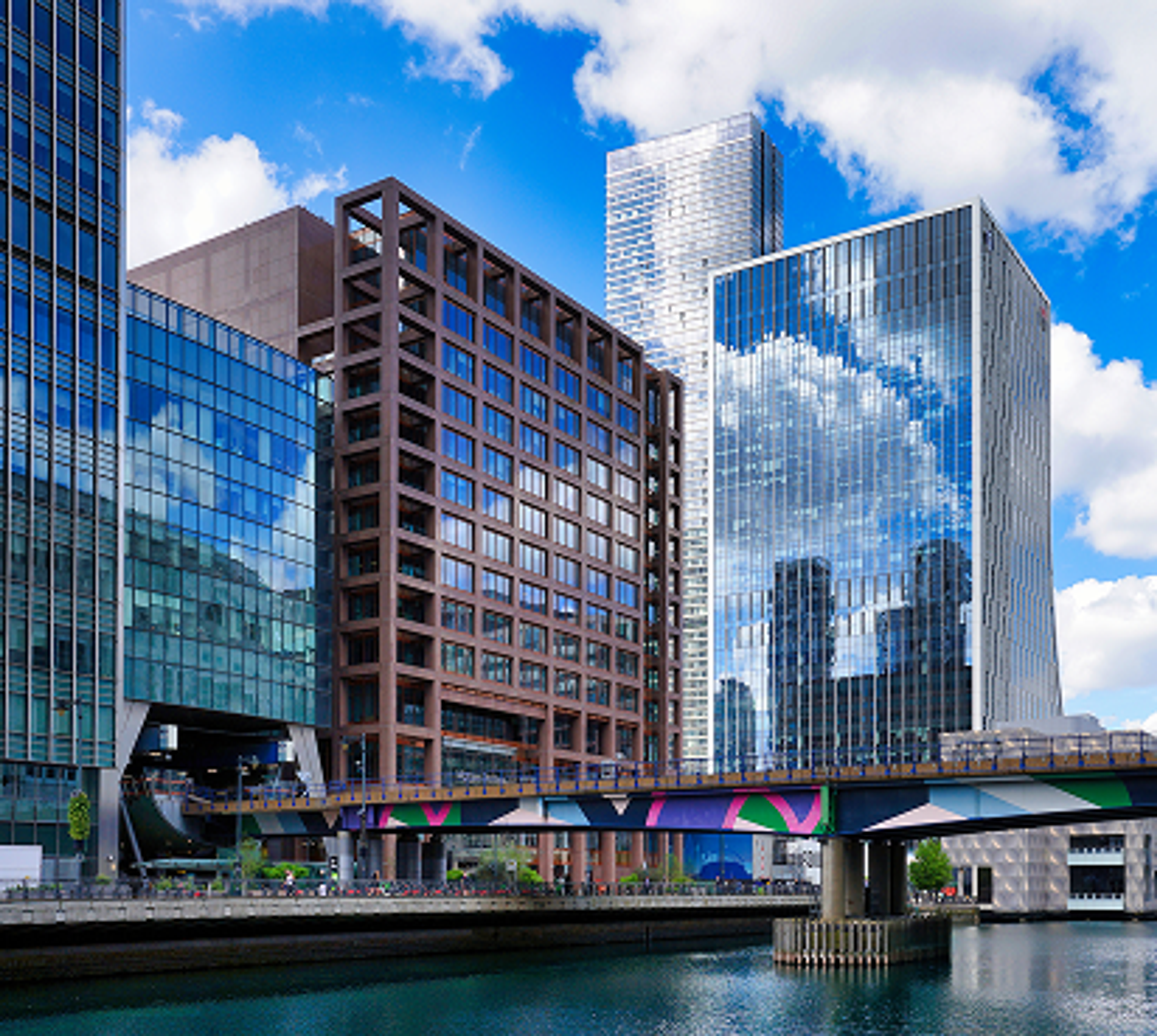 Modern glass office skyscrapers reflected in the water of a city harbor under a blue sky
