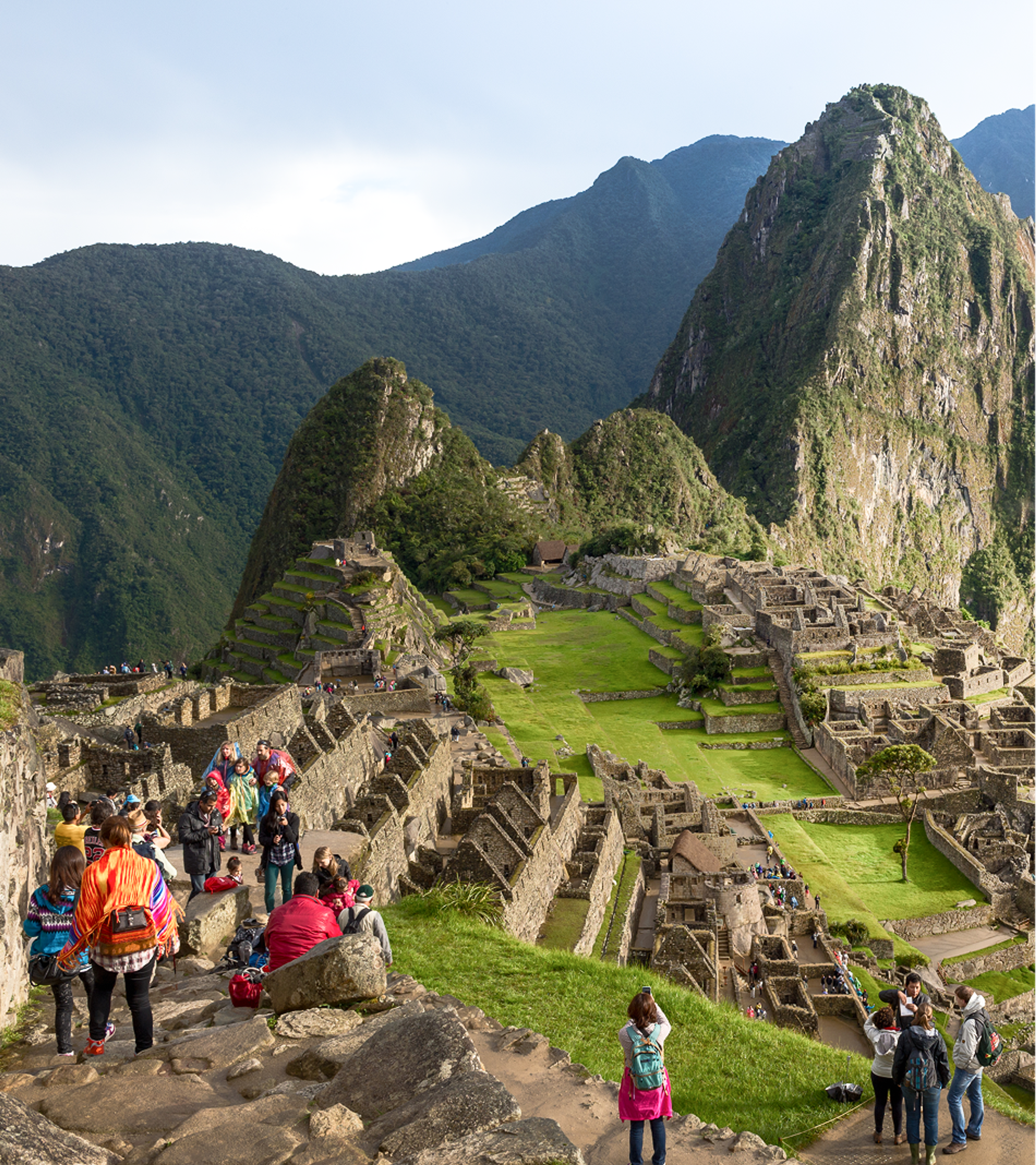 Visitors exploring the stone ruins and green terraces of Machu Picchu, surrounded by steep mountains in Peru.