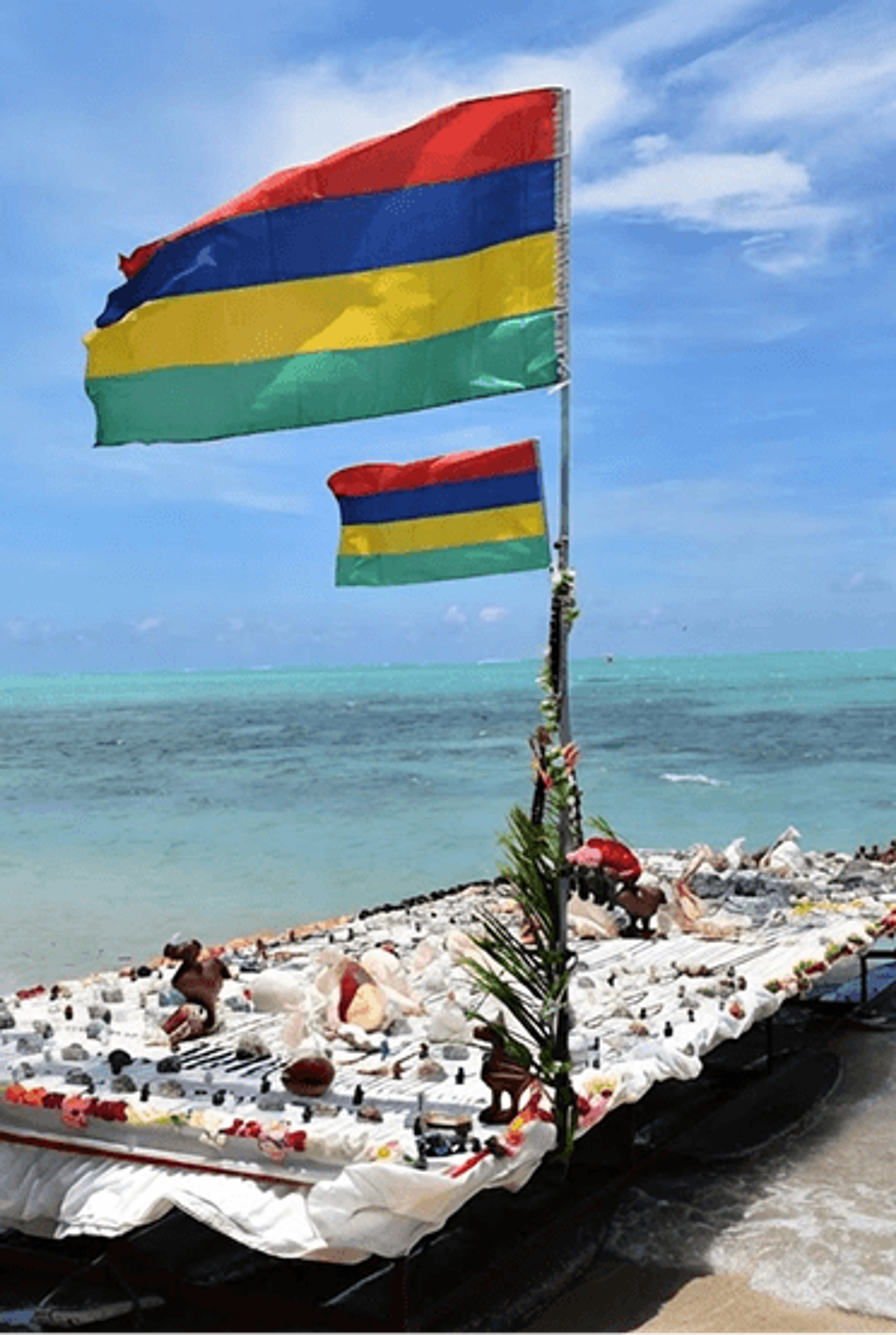 A boat flying the national flag of Mauritius near a sandy tropical beach.
