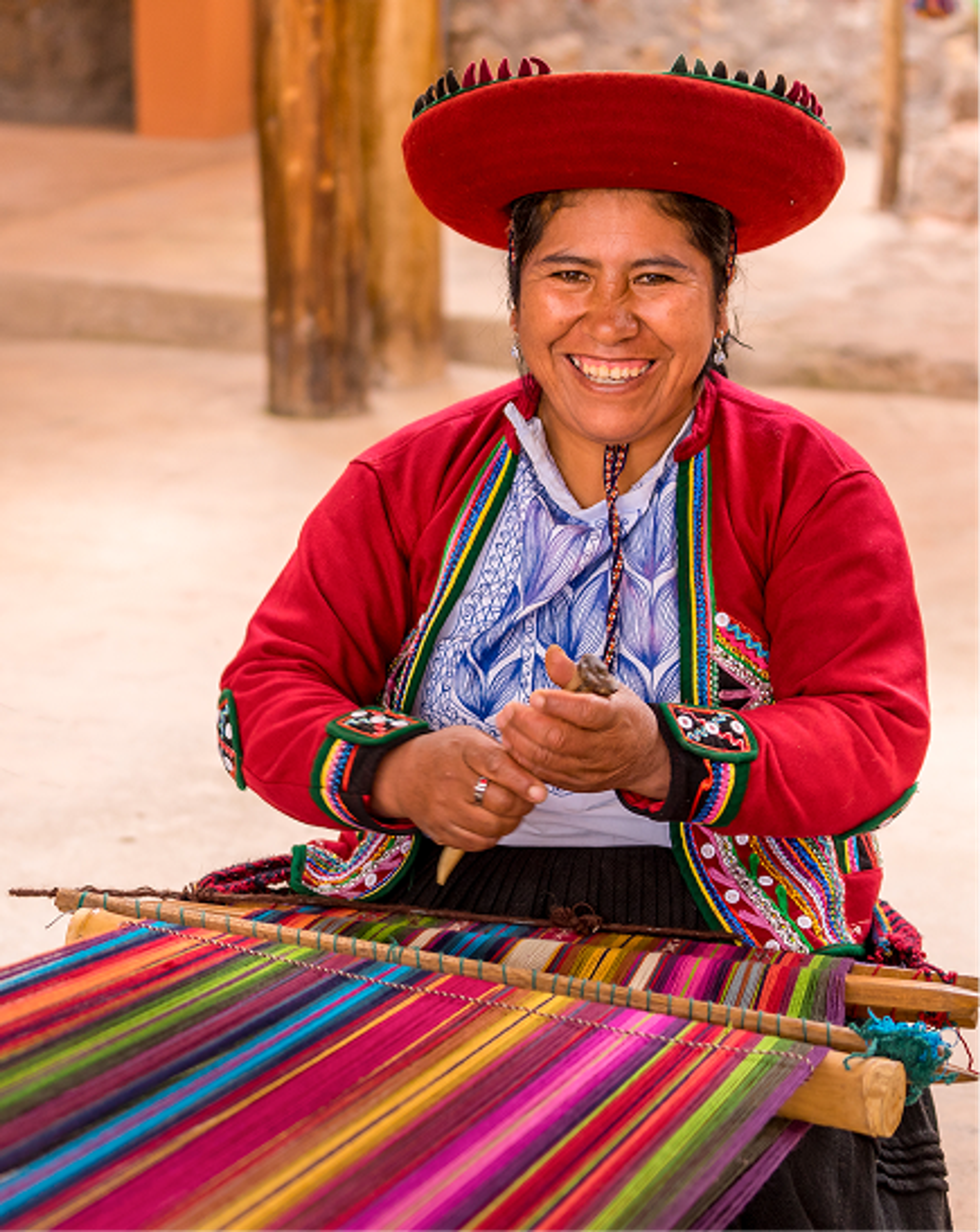 Smiling artisan in traditional dress weaving a brightly coloured textile.