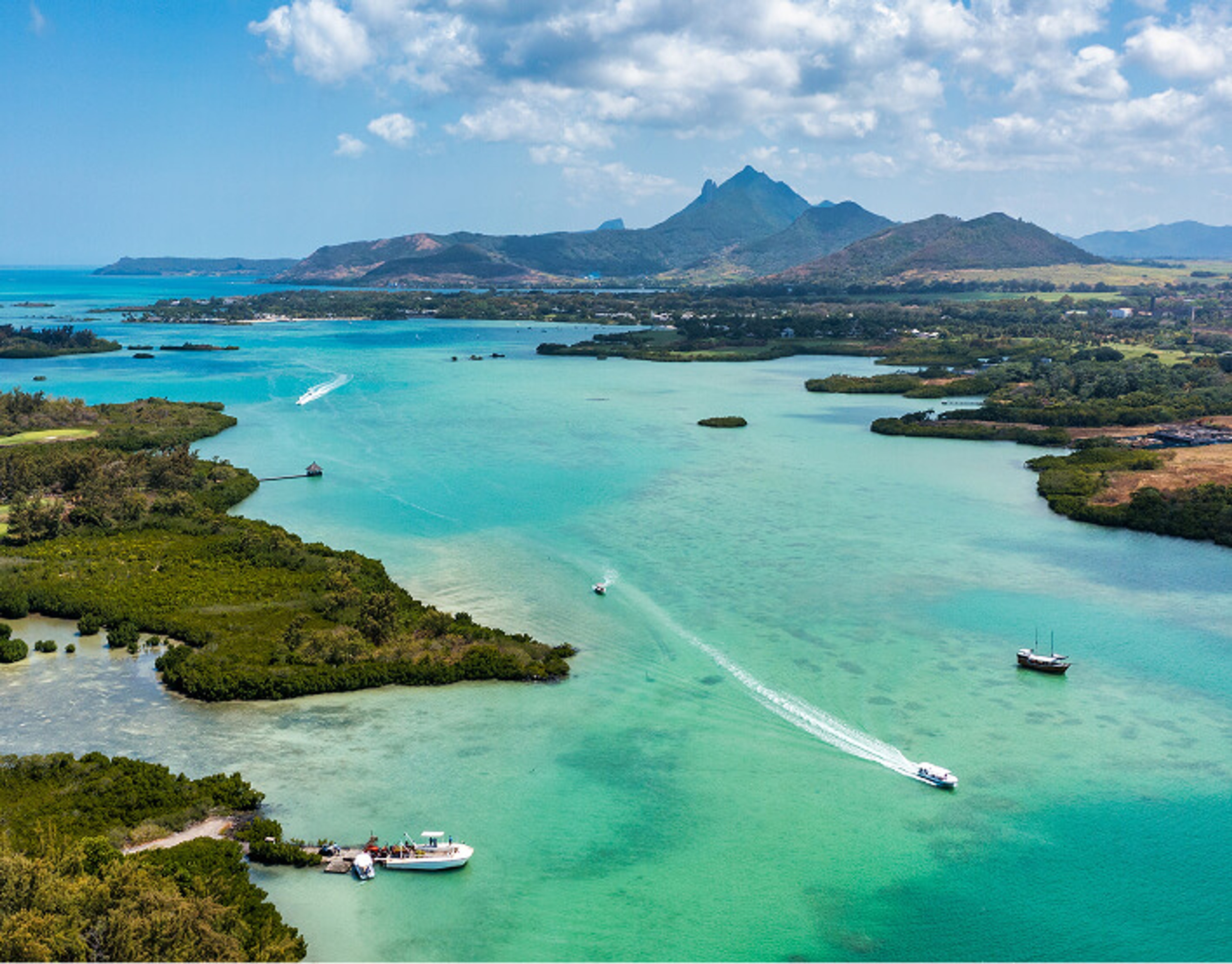 Aerial view of boats navigating clear turquoise ocean waters near tropical islands and mountains.