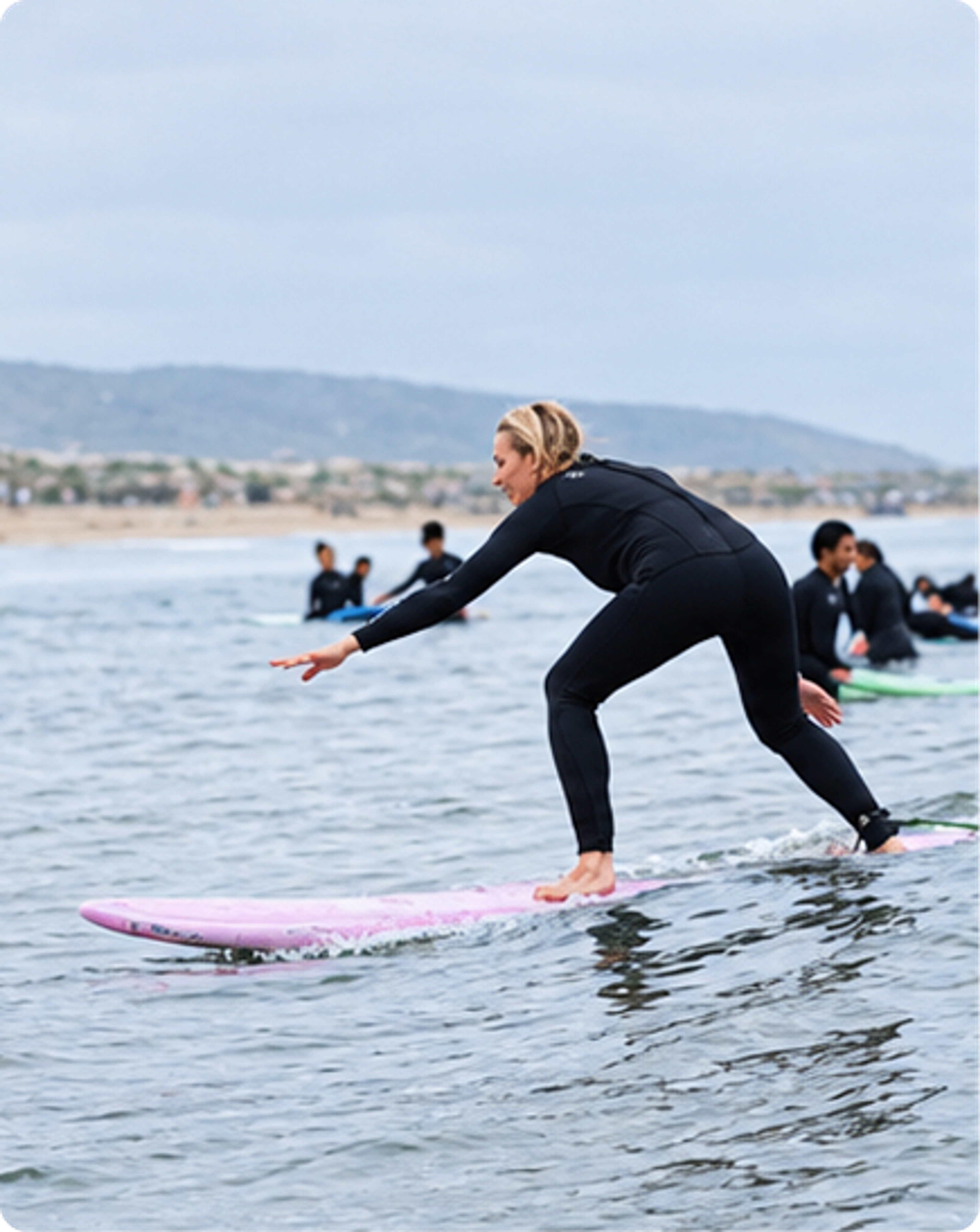 Guest balancing on a pink surfboard during a group surf lesson.