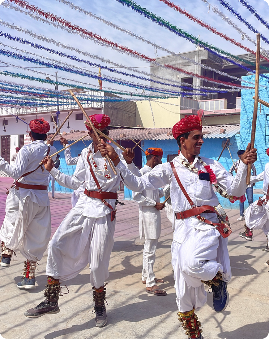 Traditional dancers in white outfits and red turbans performing with wooden sticks.