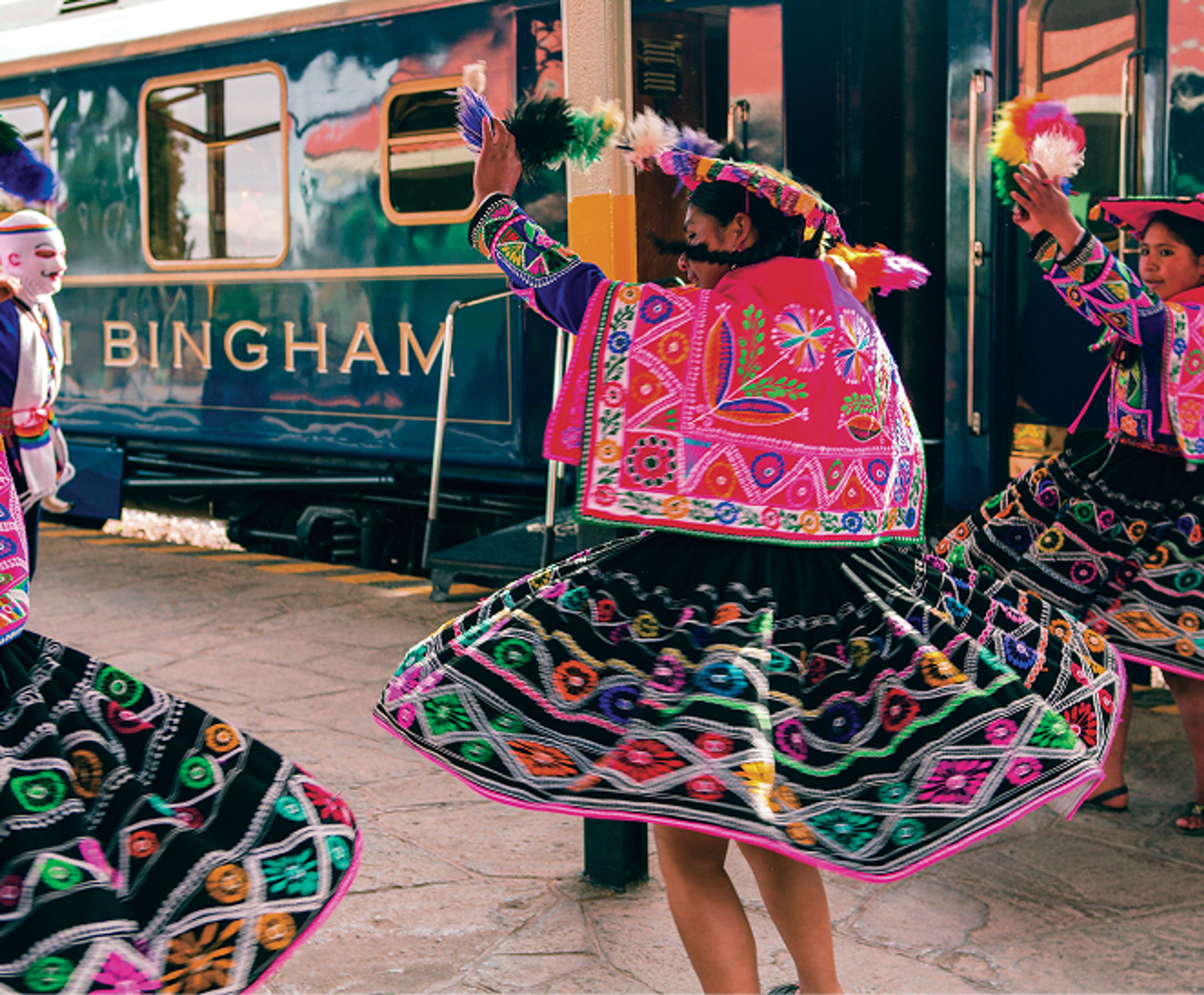 Dancers in colourful embroidered costumes performing beside the Hiram Bingham train.