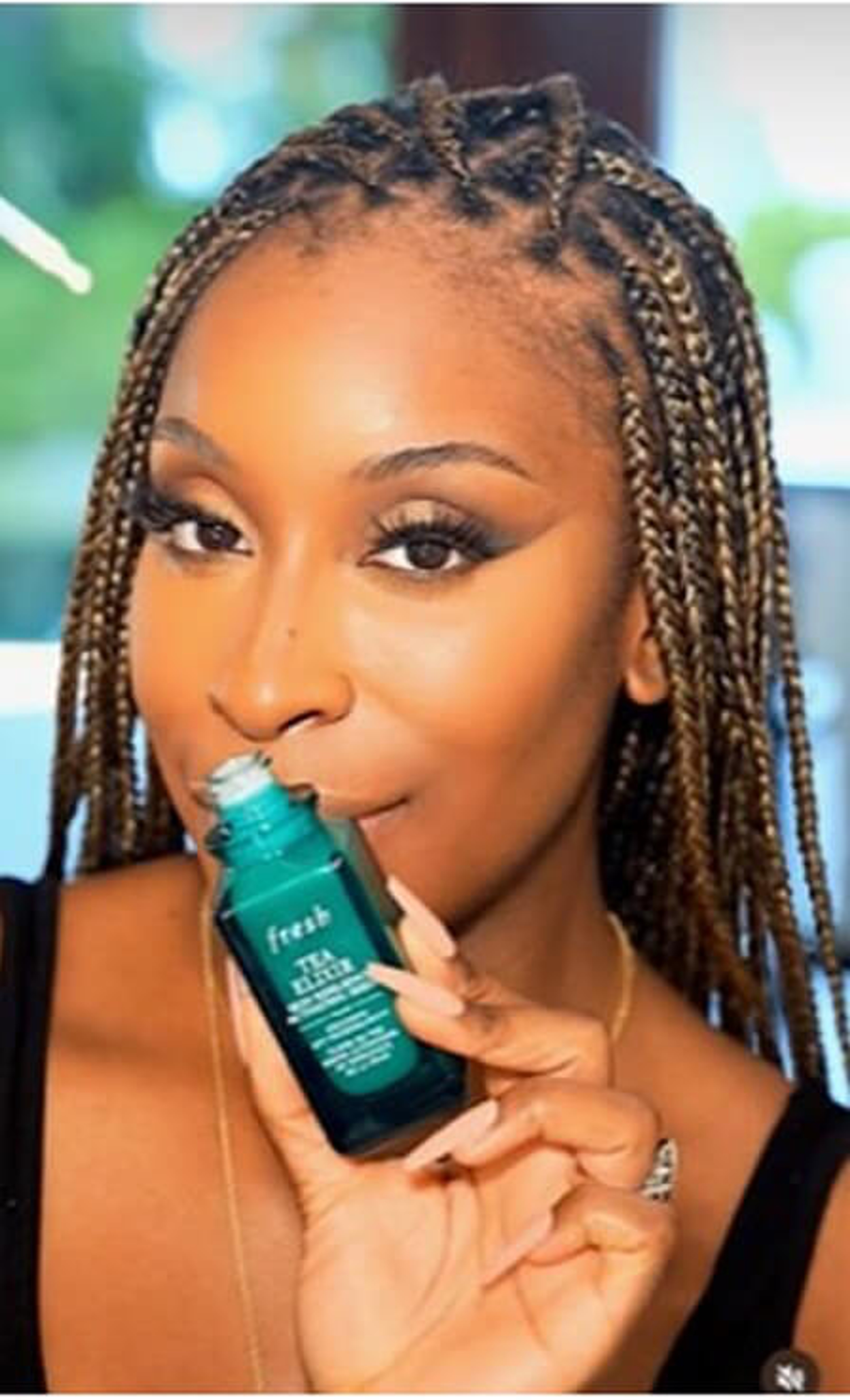 A woman with braided hair holding a bottle of Fresh Tea Elixir serum near her face