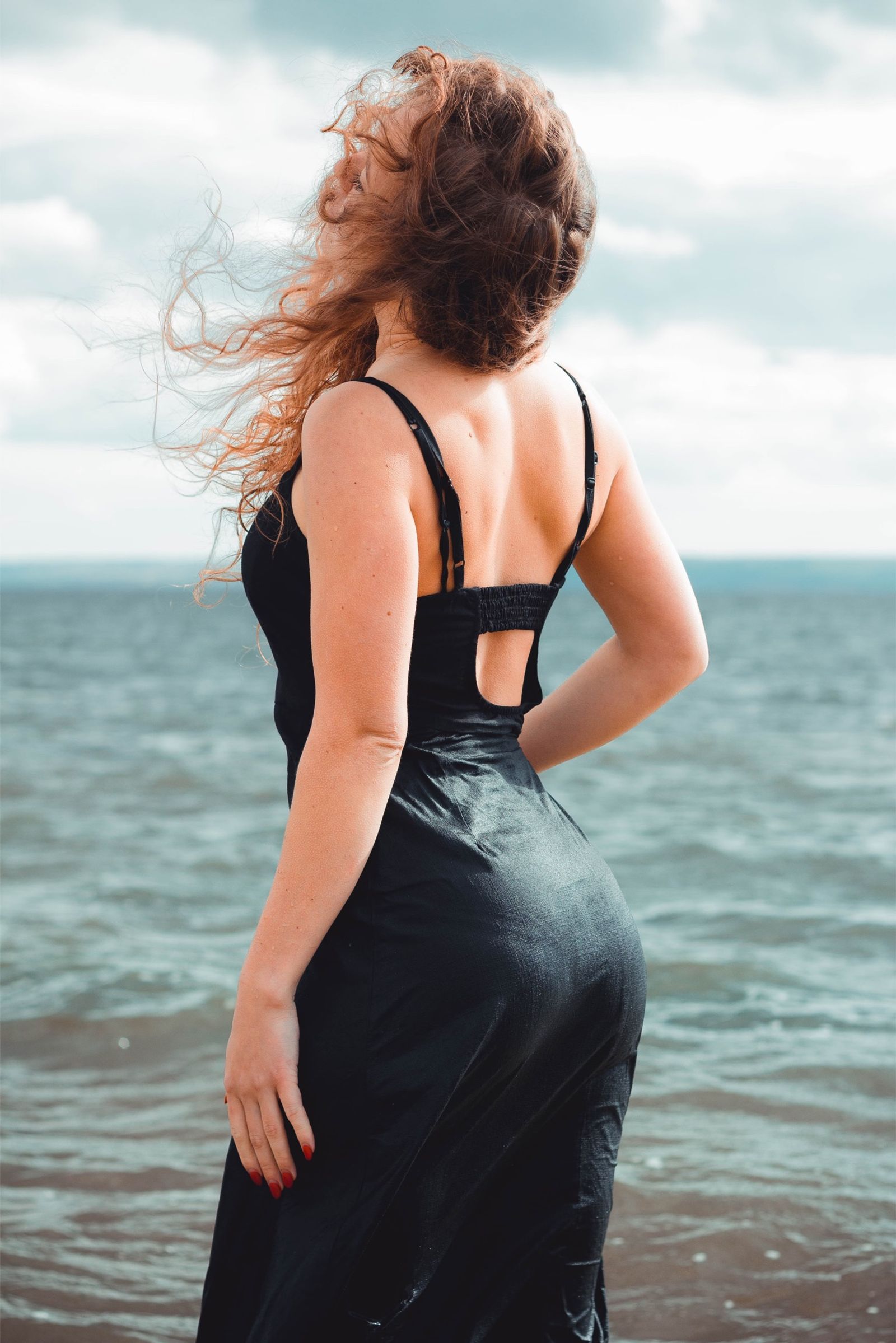 Woman in a black dress by the sea, hair in the wind