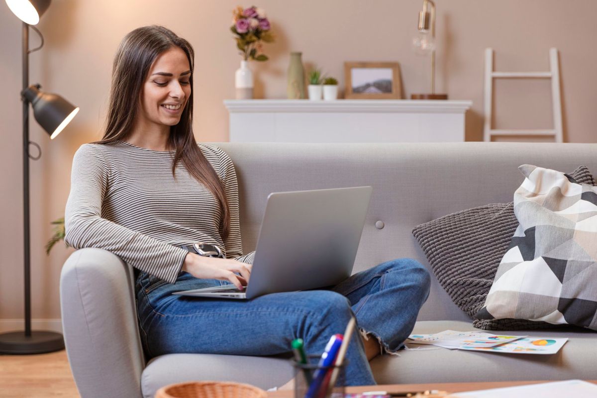 young-woman-working-on-laptop-while-sitting-on-grey-sofa
