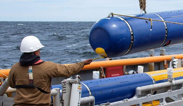 A man moving cylindrical equipment on a ship